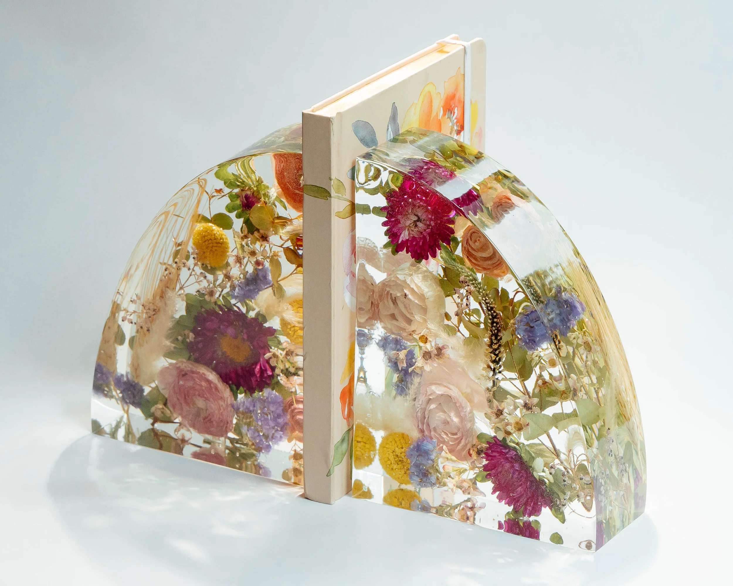 A transparent acrylic artwork with embedded flowers, leaves, and botanical elements, set against a plain light background.