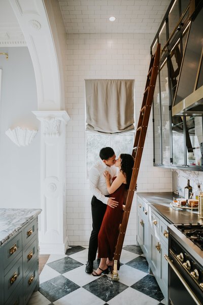 A couple kissing in a kitchen with a loft ladder and white brick walls.