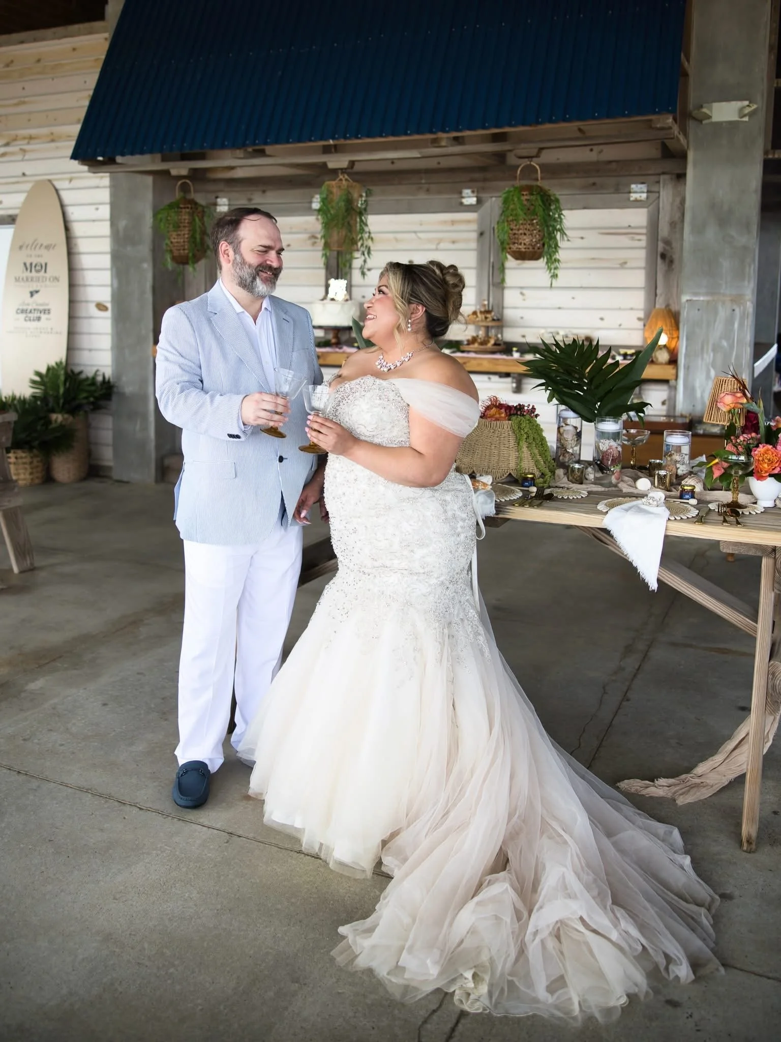 A bride and groom toasting at their wedding reception indoors, with rustic decor including greenery and wooden elements.