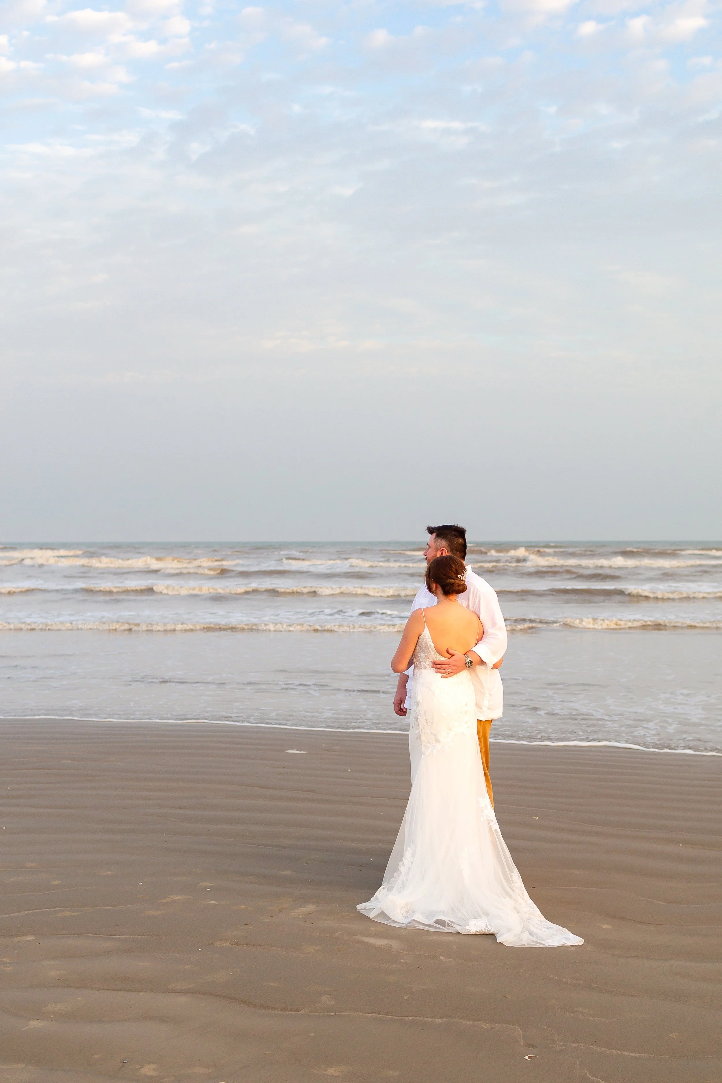Sunset portraits of newlyweds embracing along the shoreline in Galveston.