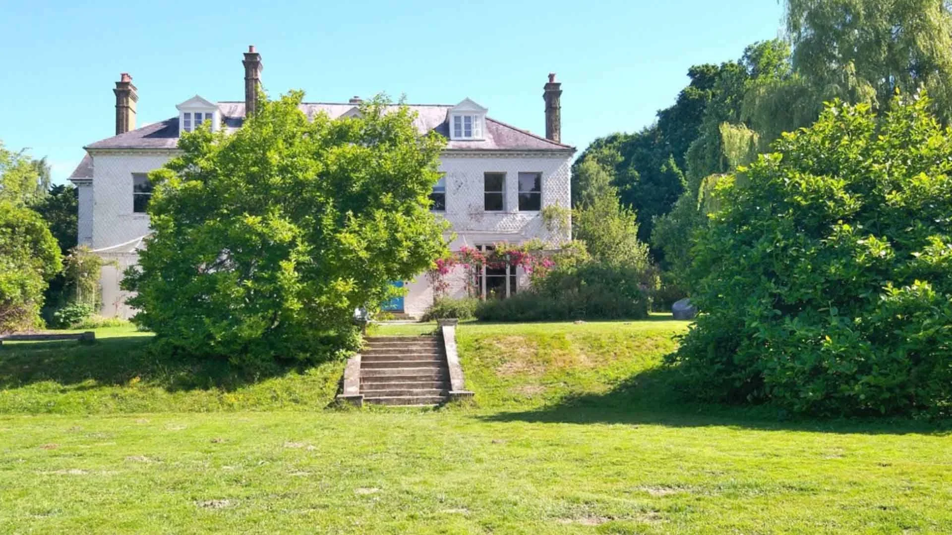 Large house with stairs leading up to it with many trees