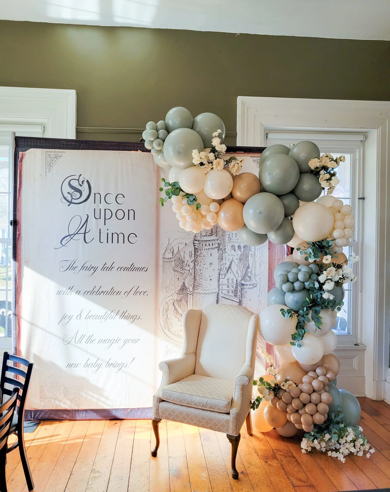 Decorative backdrop with balloons and flowers for a celebration, featuring a sign with the words "Once upon a time" and an illustration of a castle, in a room with wooden floors and window frames.