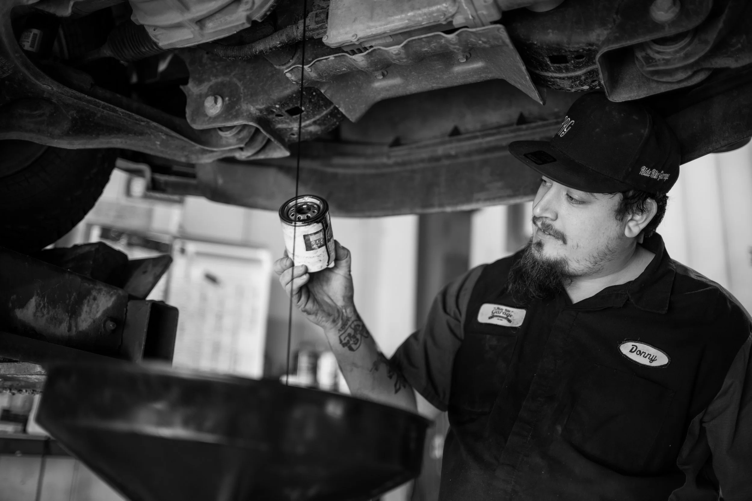 three men in ride rite mechanic shirts examine a motor in a car