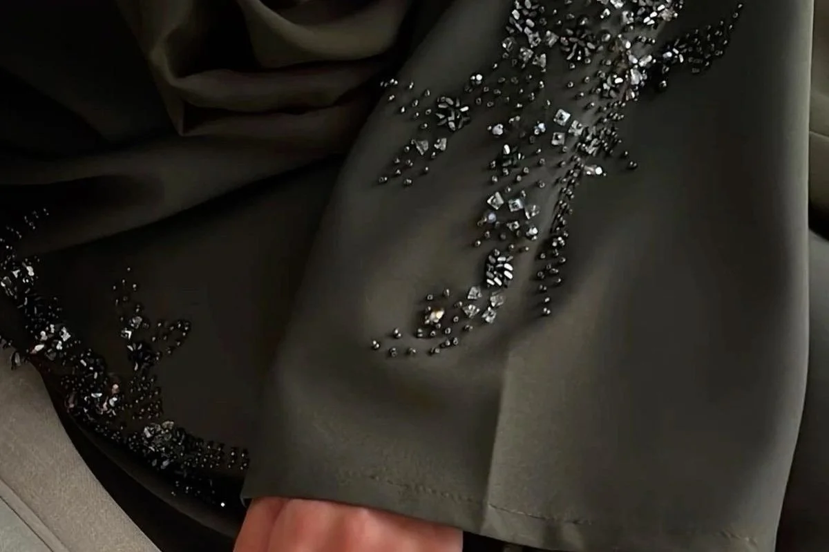 Close-up of a dark green fabric with intricate black and silver beaded embroidery and embellishments.