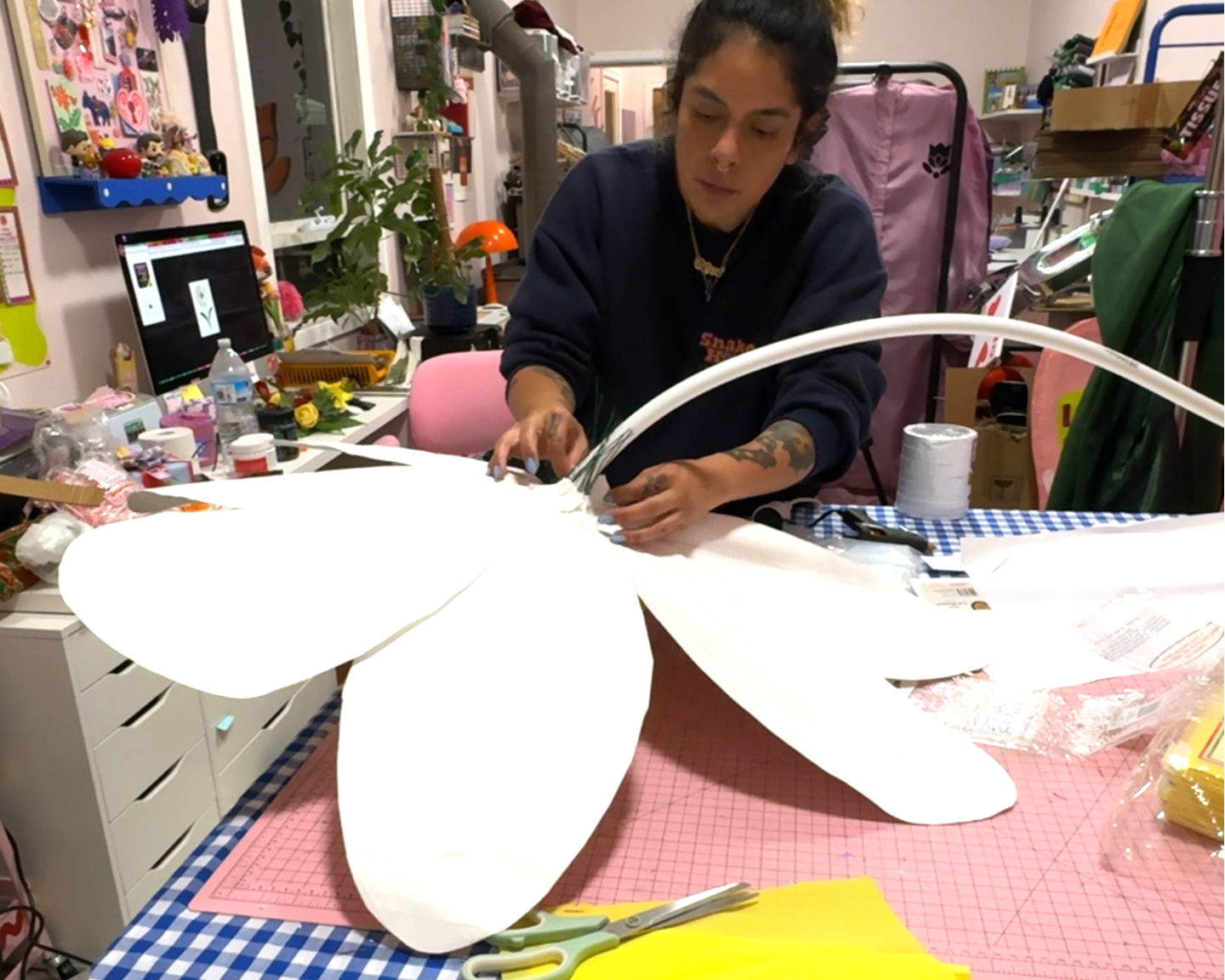 A woman assembles a giant daisy prop in a messy studio