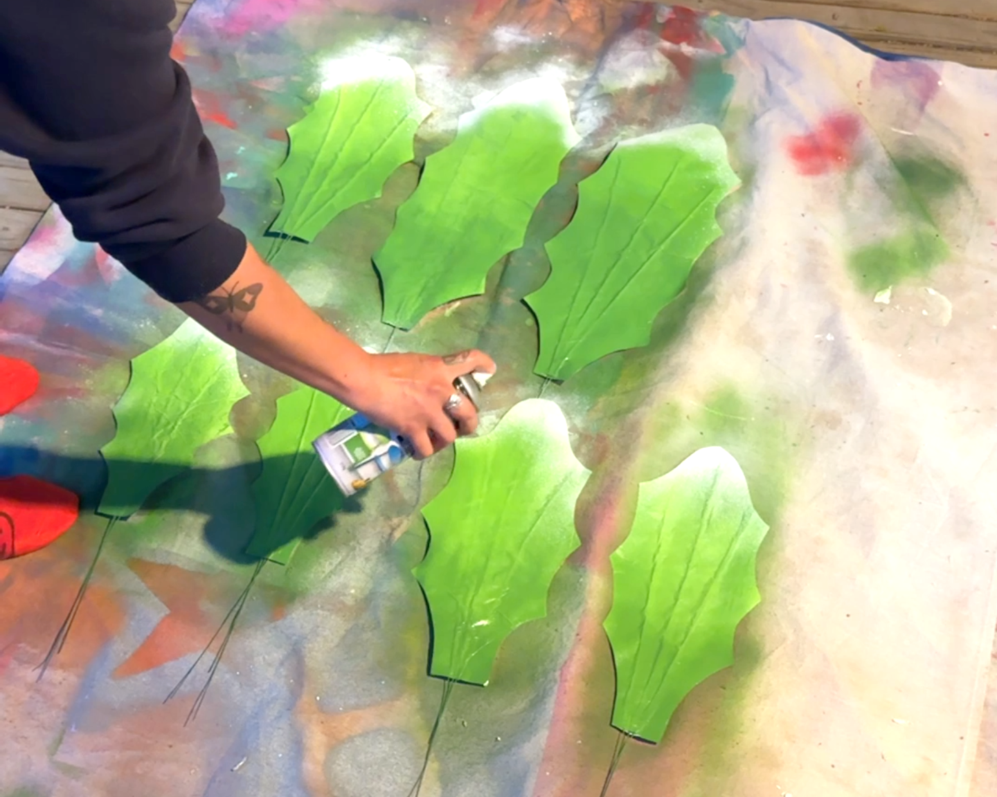 A woman's hands spray white cutout leaves for a giant daisy prop with white spray paint