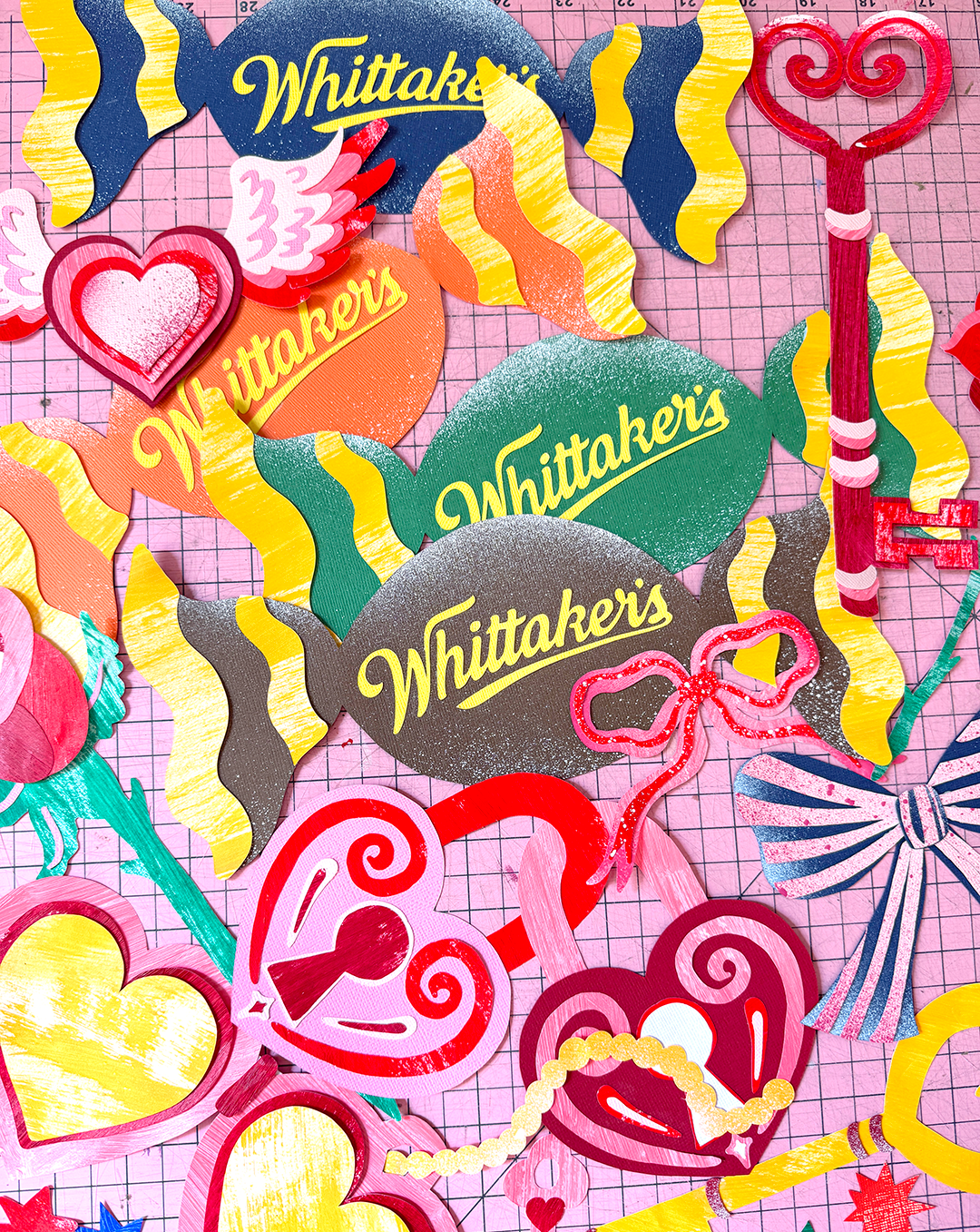 A birds-eye-view collection of collaged Valentine's Day themed illustrations made by Kitiya Palaskas sit on a pink cutting mat.