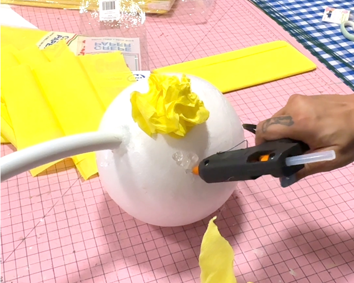A woman's hand glues scrunched up yellow crepe paper onto a large styrofoam ball for a giant daisy prop