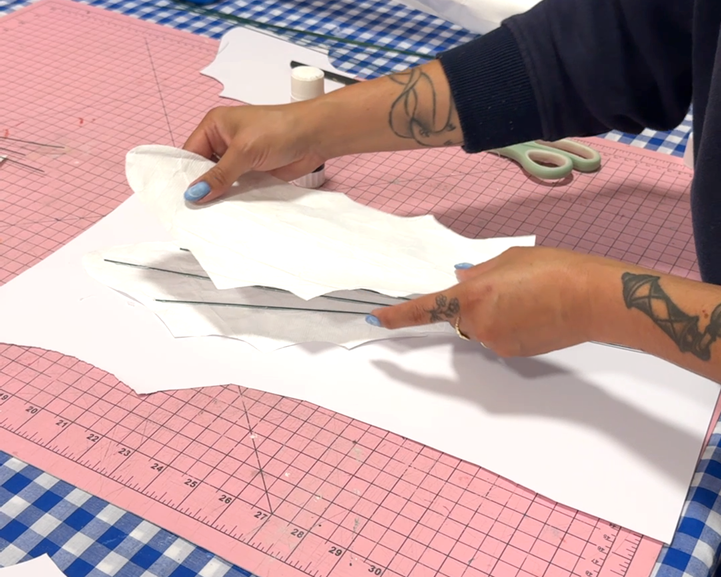 A woman's hands glue florist wire onto a white cutout leaf shape using hot glue for a giant daisy prop.
