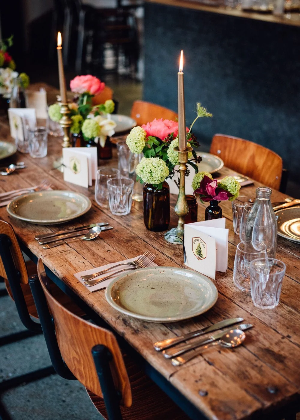 A rustic wooden table set for a formal dinner with floral centerpieces, candles, glassware, and plates.