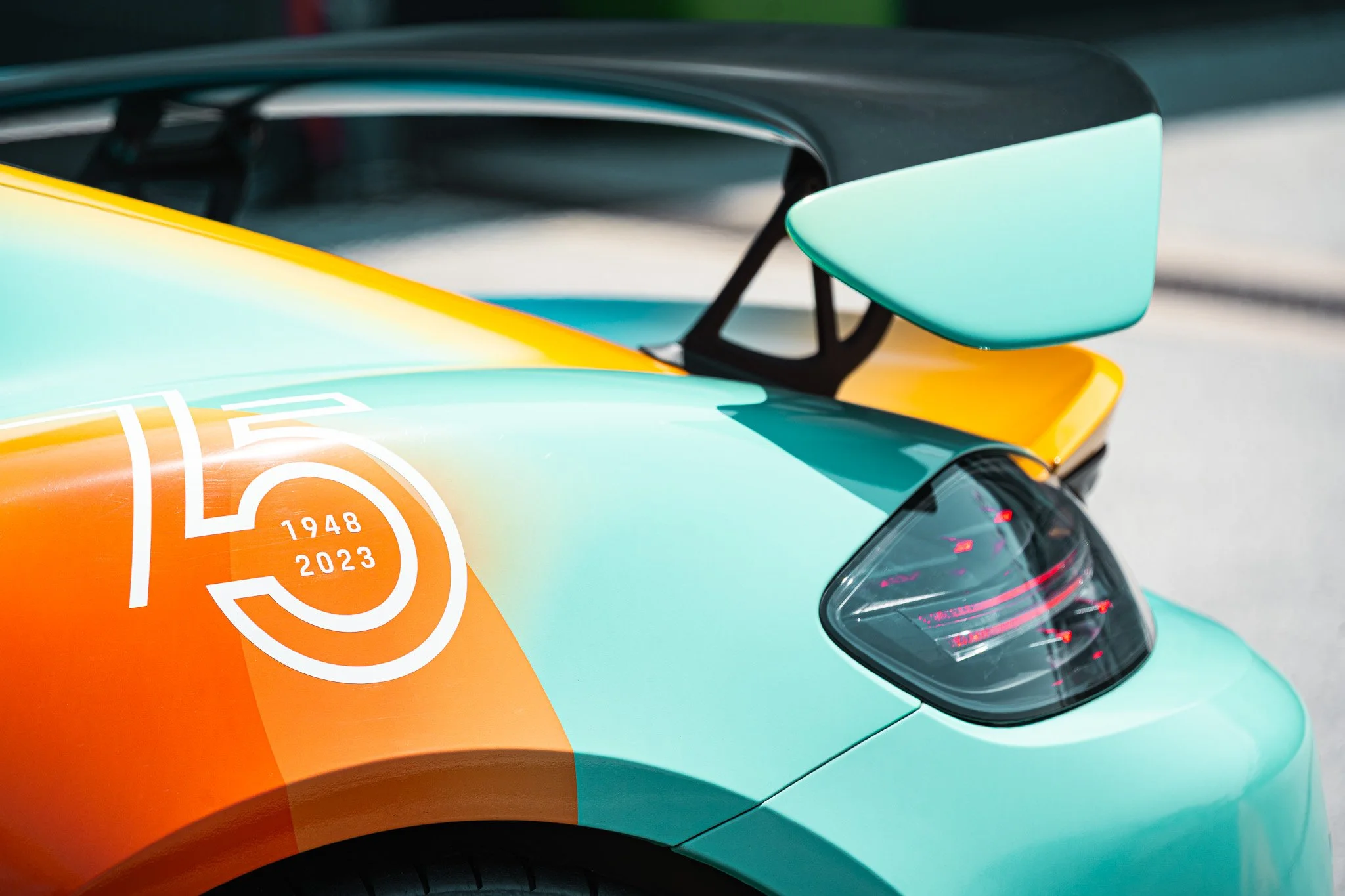 Close-up of a sports car with a colorful gradient paint job featuring a 75th anniversary logo celebrating 75 years from 1948 to 2023 on the side, and a teal rear wing.