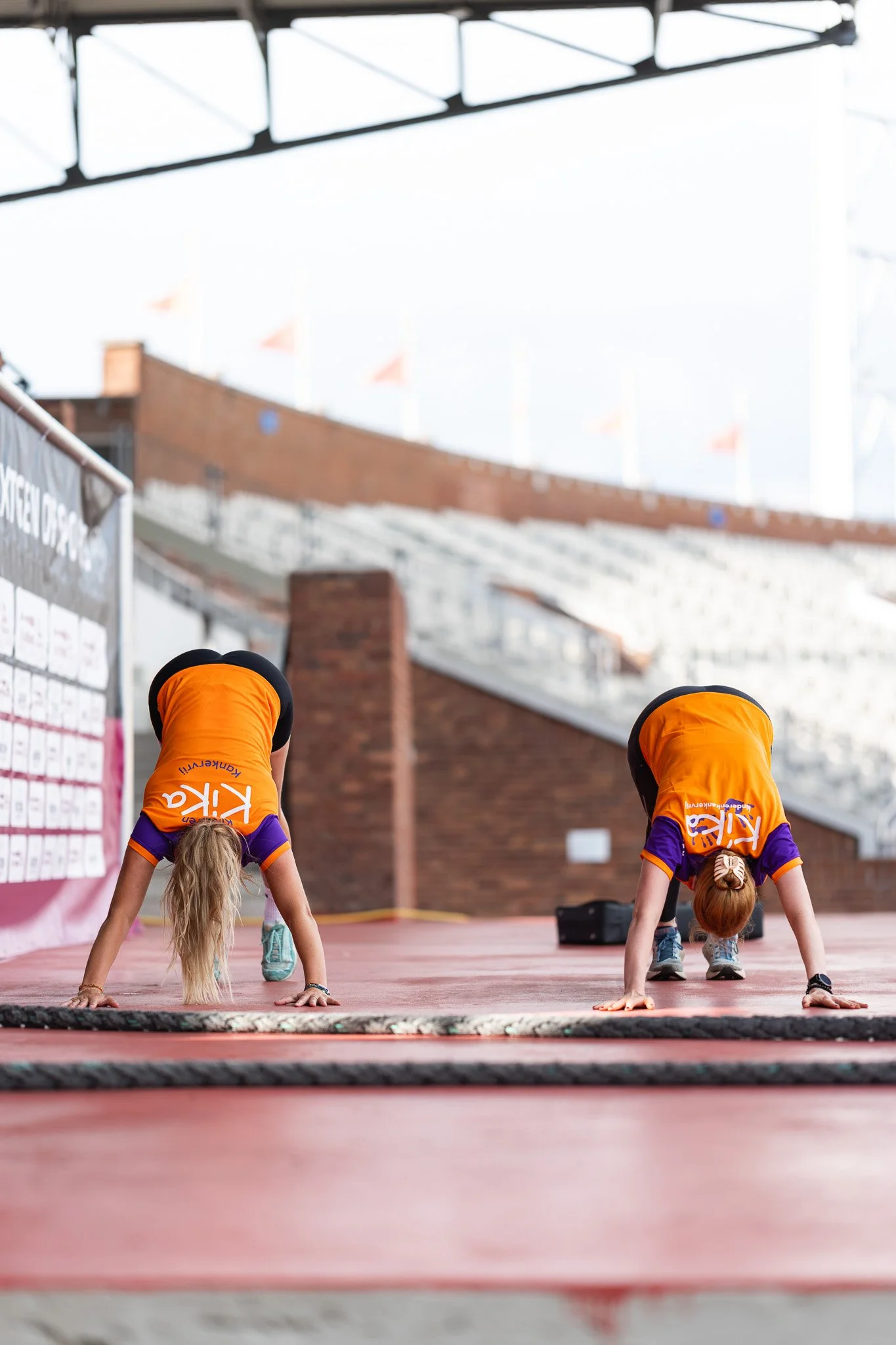 Twee jonge vrouwen in sportkleding doen handstand op een volleyballoft in een sporthal.