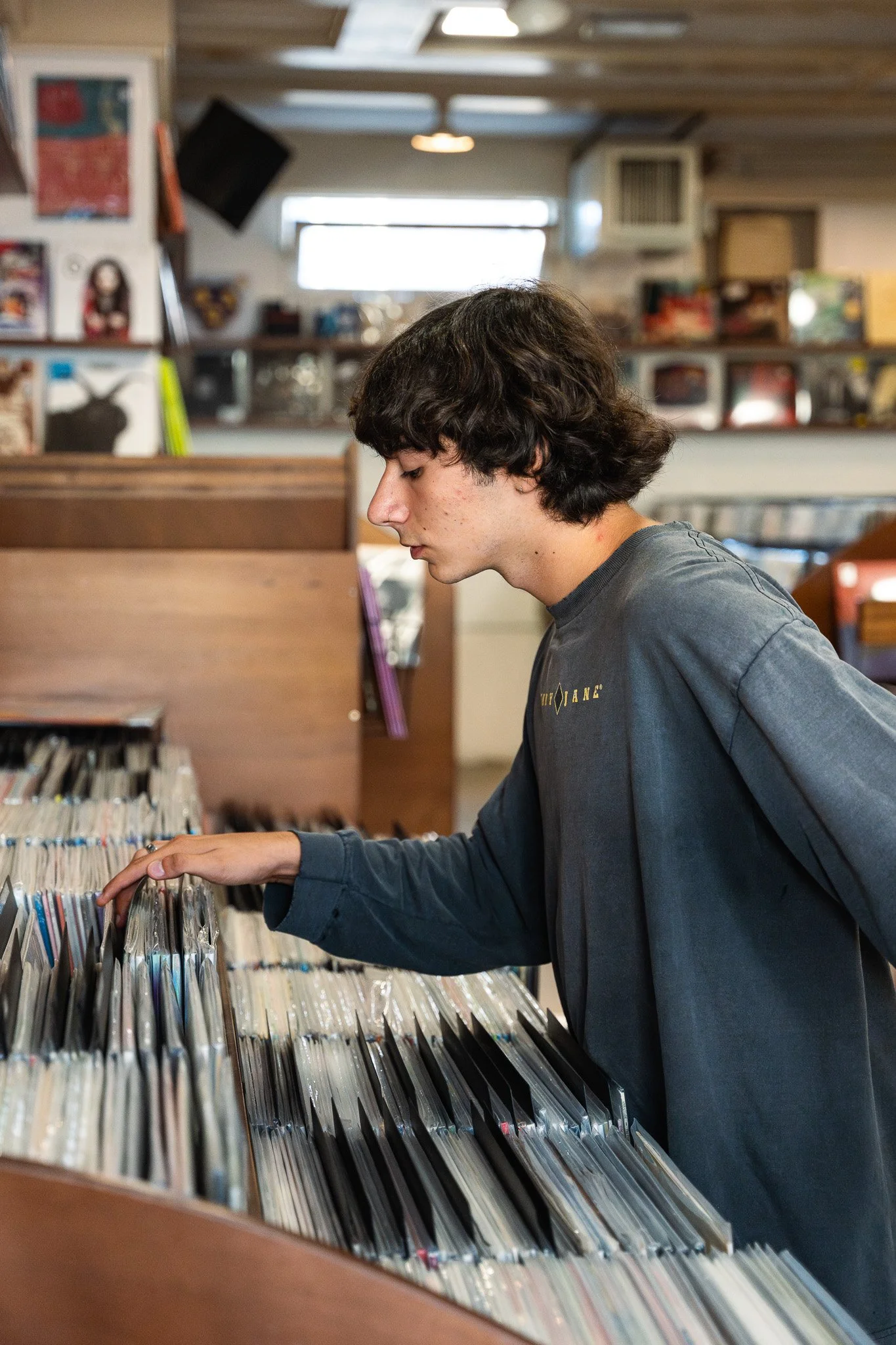 A young man with dark, wavy hair browsing through vinyl records at a record store.