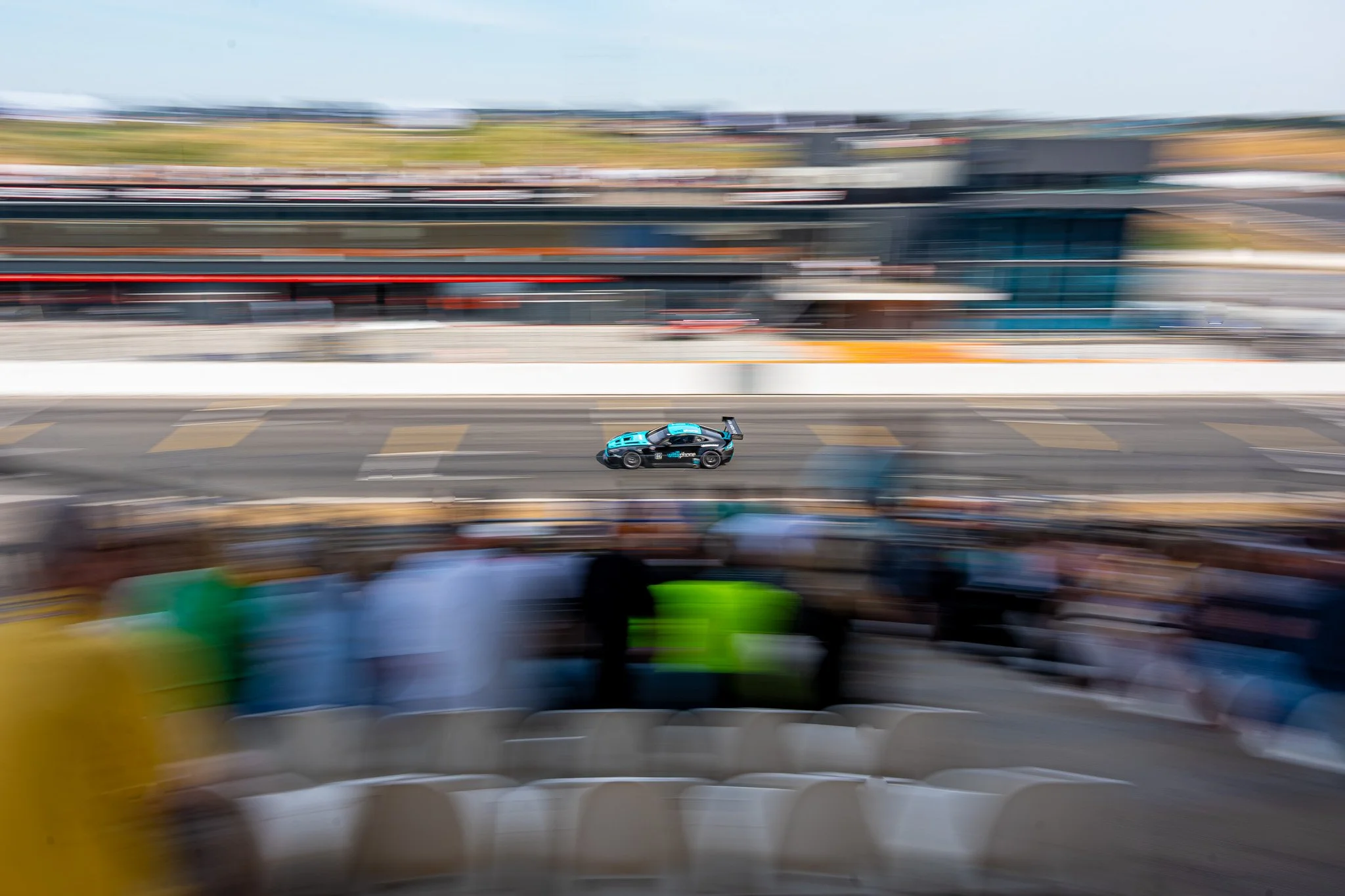 Een raceauto rijdt op een circuit met een snelheidsbeweging op de foto, terwijl de achtergrond wazig is door de snelheid.