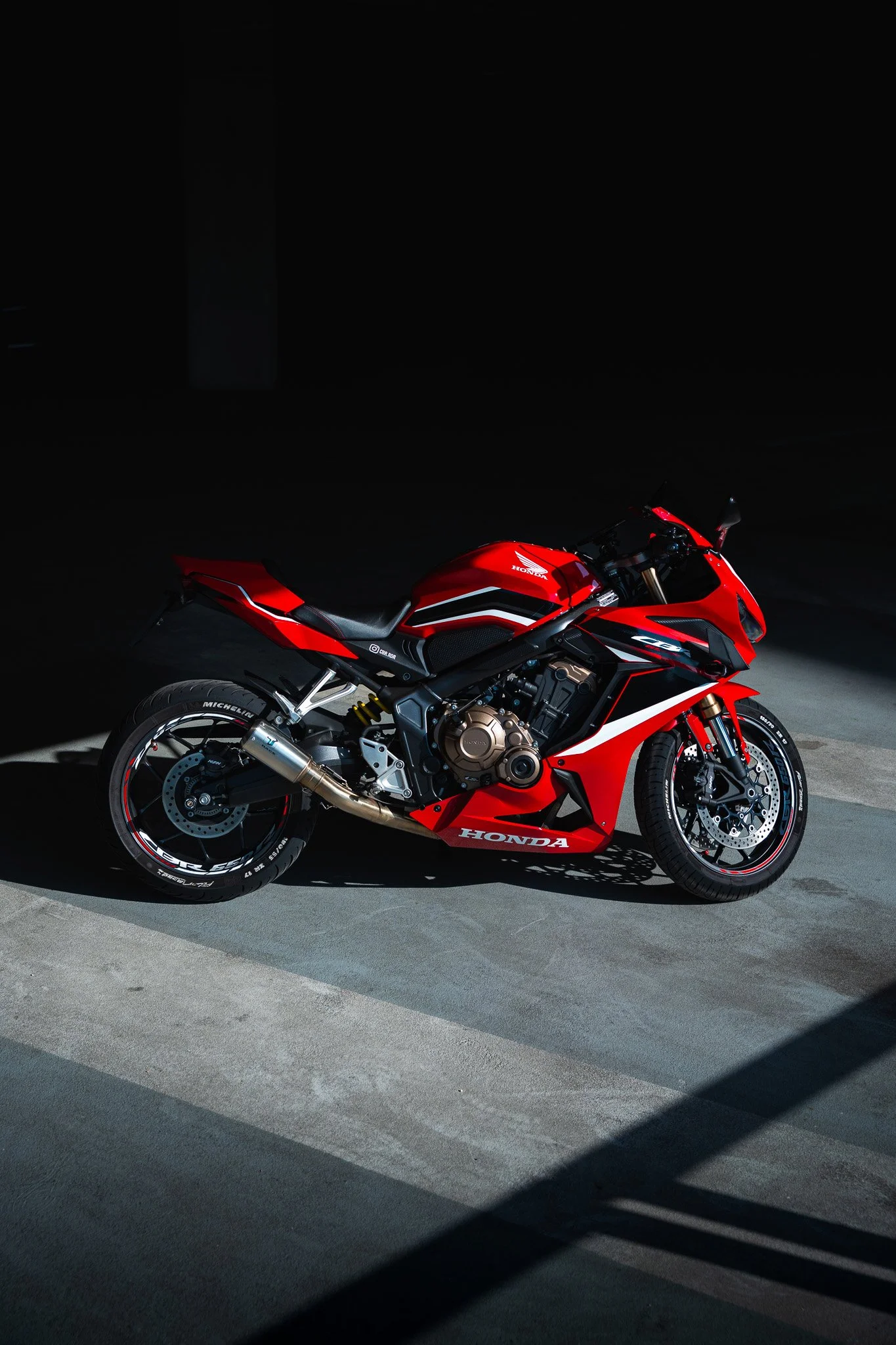 Red Honda sport motorcycle with black and white accents parked on a concrete surface in a dimly lit environment.