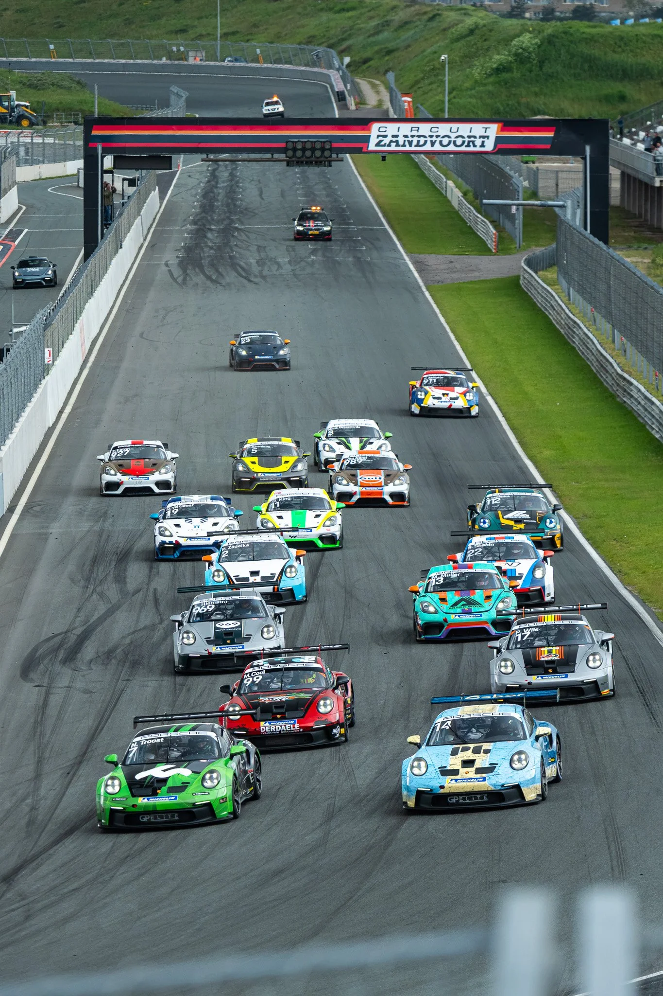Raceauto's op een circuit met veel verschillende kleuren en modellen, vlak voor de start of finishlijn.