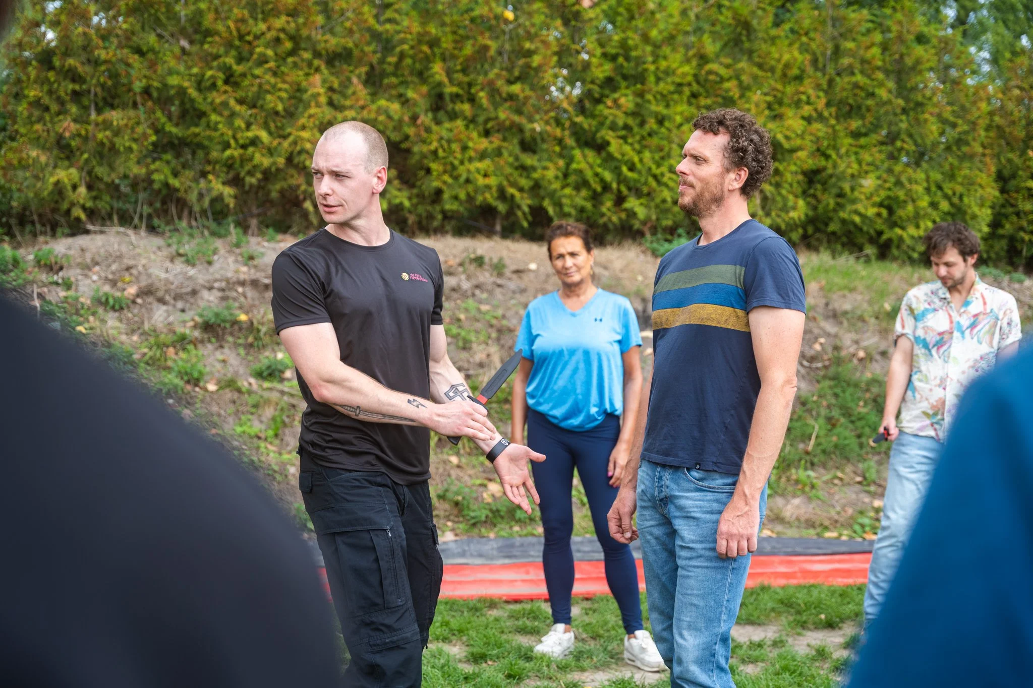 Een groep mensen die een handdruk uitwisselen tijdens een buitenbijeenkomst in een park, met bomen op de achtergrond.