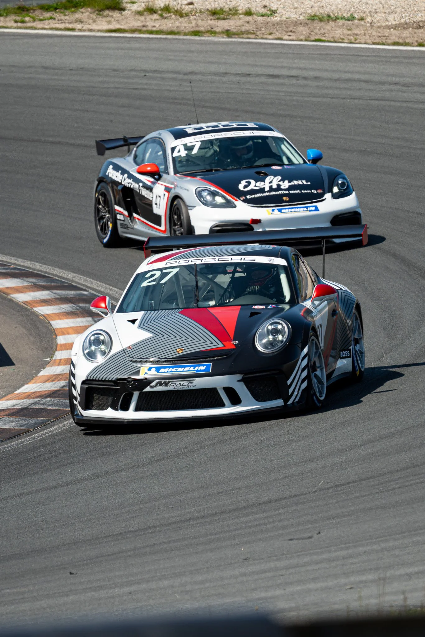 Twee raceauto's op een racebaan, een Porsche en een andere sportauto, in een bocht.