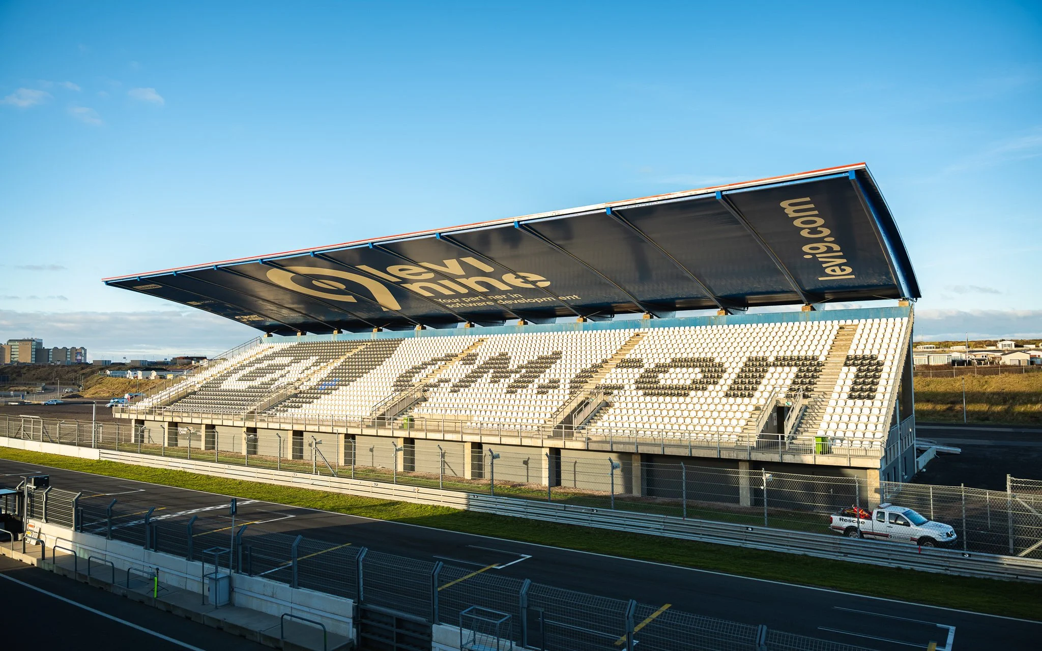 Leeg circuitracecircuit met wit en zwarte tribunekaarten onder een grote zwarte overkapping, onder een blauwe lucht.
