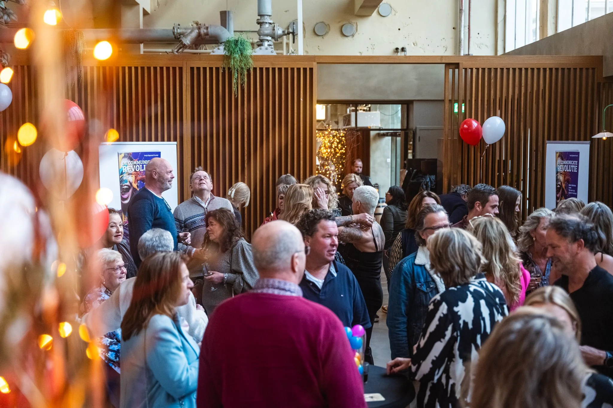 Een groep mensen die samen in een binnenruimte staan, met feestballonnen en decoraties, waarschijnlijk tijdens een evenement of bijeenkomst.
