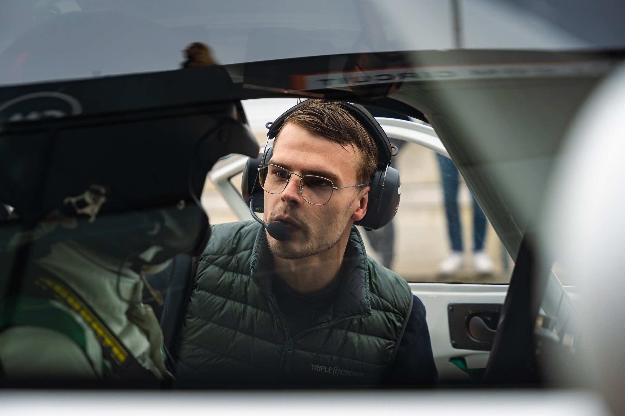 Man in pilotenoutfit en koptelefoon, die naar zijn co-piloot kijkt in de cockpit van een vliegtuig.