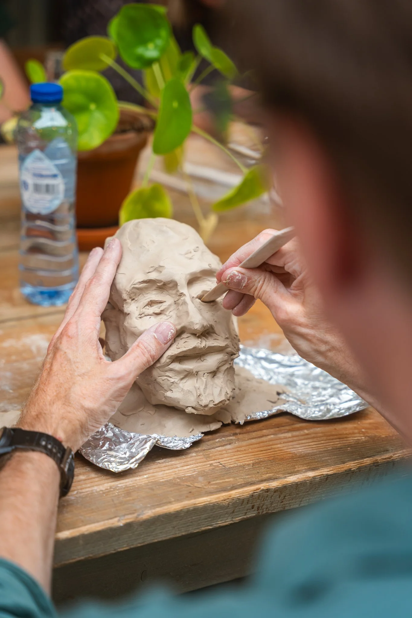 Persoon boetseert een papieren schedel op een houten tafel, met een plantenpot op de achtergrond.