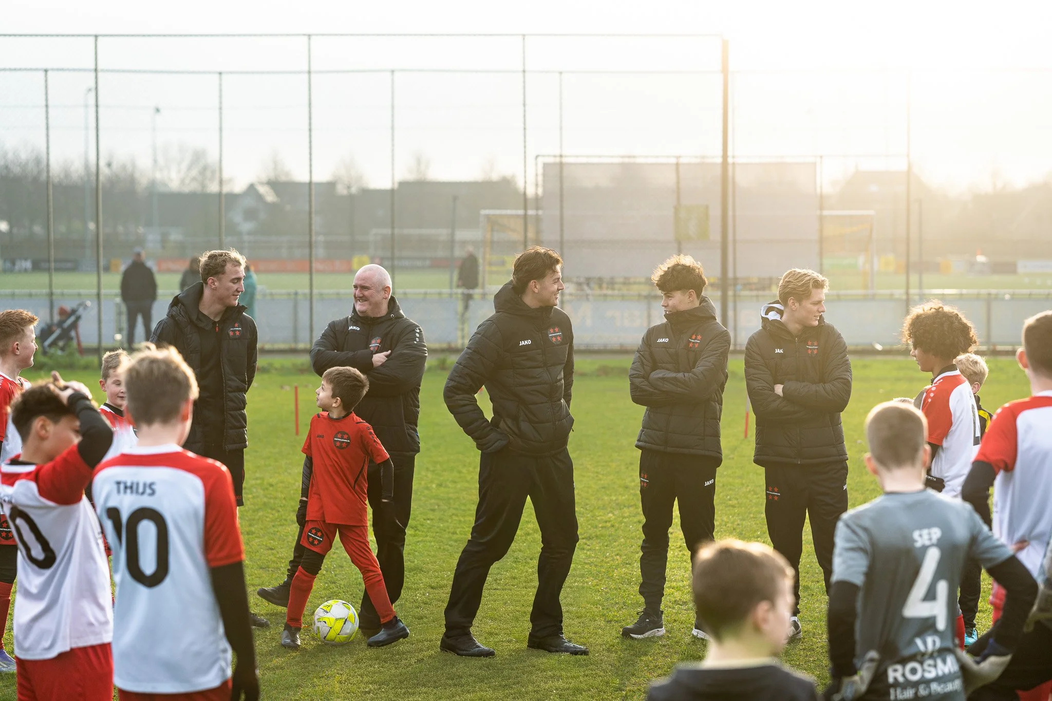 Young soccer players and coaches standing on a field chatting with the sun setting in the background.