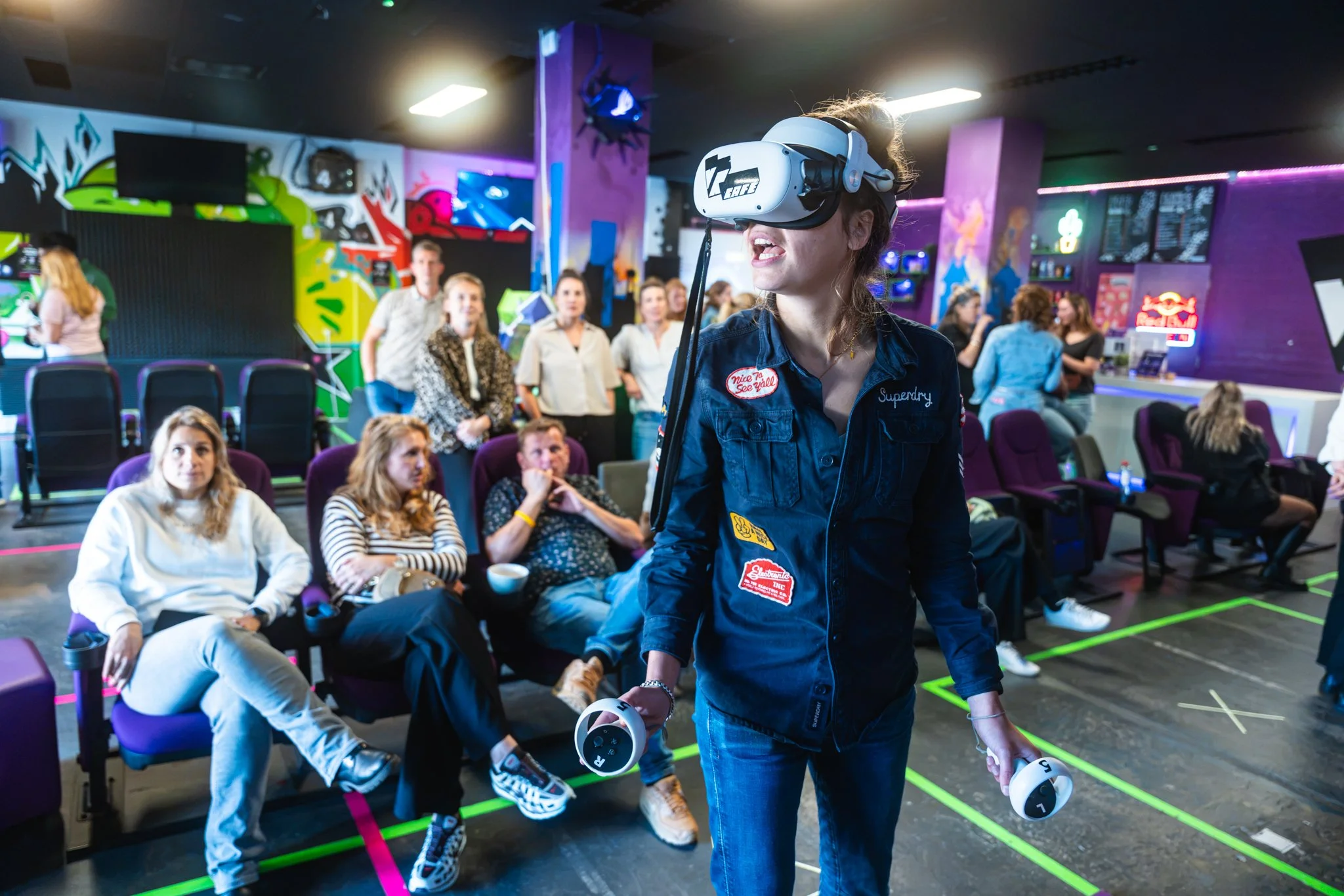 Een vrouw met een virtual reality-hoofdlampje en een VR-controller in een groep mensen in een entertainmentcentrum.