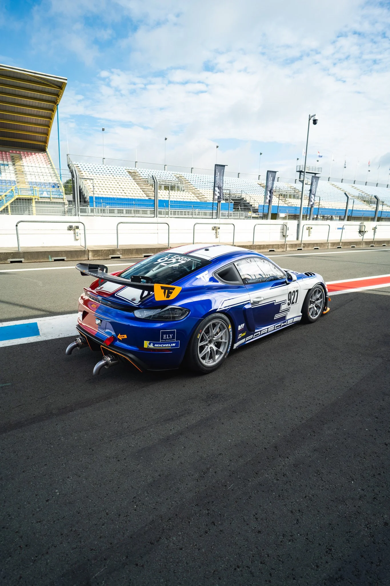 Een raceauto op een circuit met lege tribunes en een blauwe lucht met wolken.