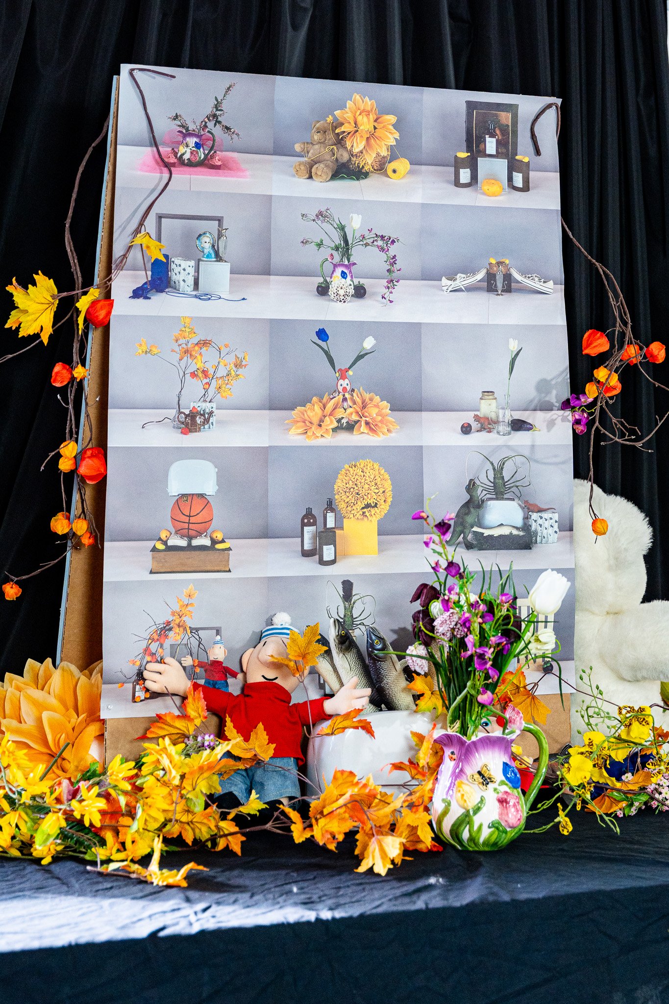 Colorful display with a poster of various decorated objects and toys, surrounded by artificial autumn leaves, flowers, and a plush bunny on the right.