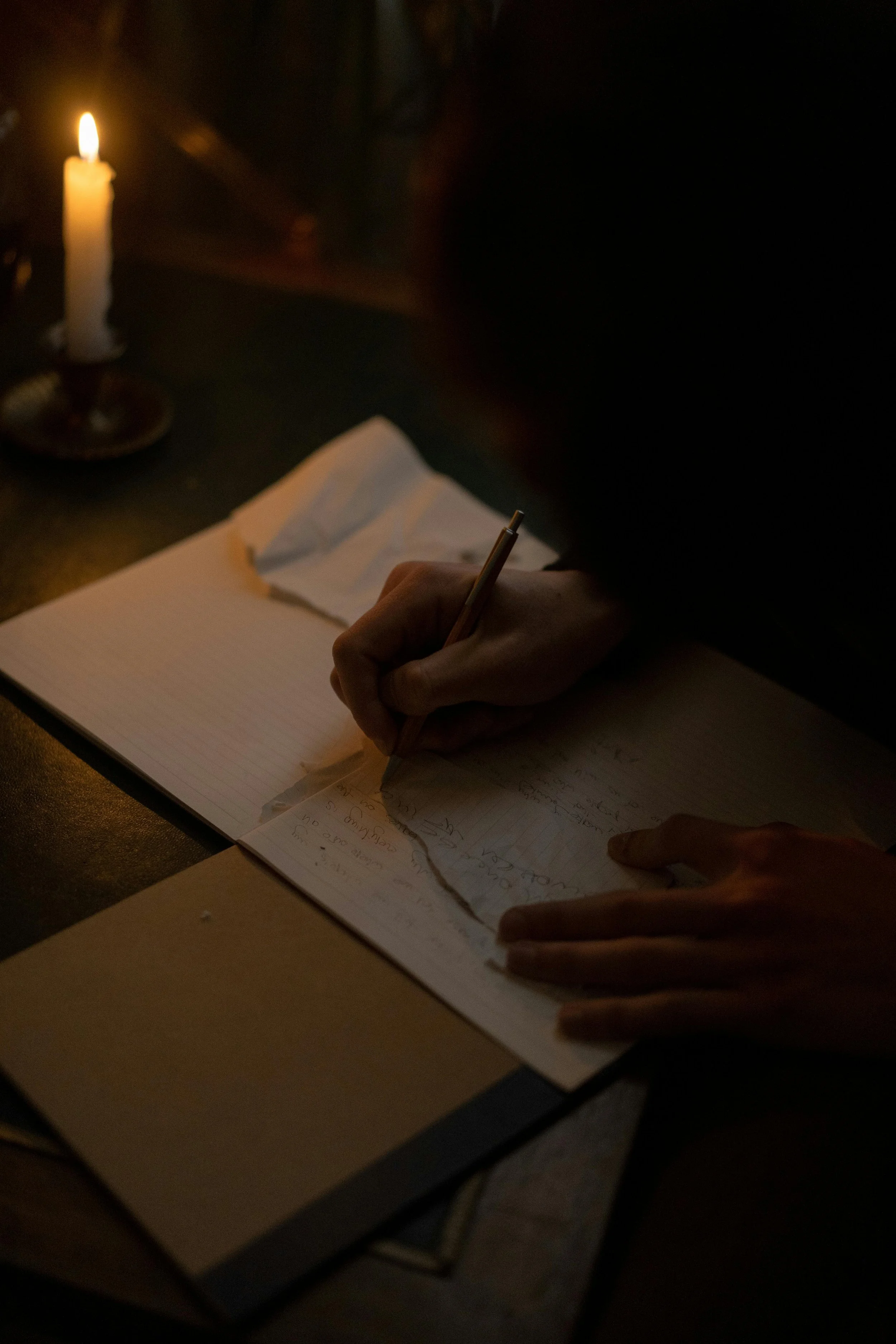 Hands writing in a notebook beside candlelight, reflecting quiet reflection and disciplined growth.