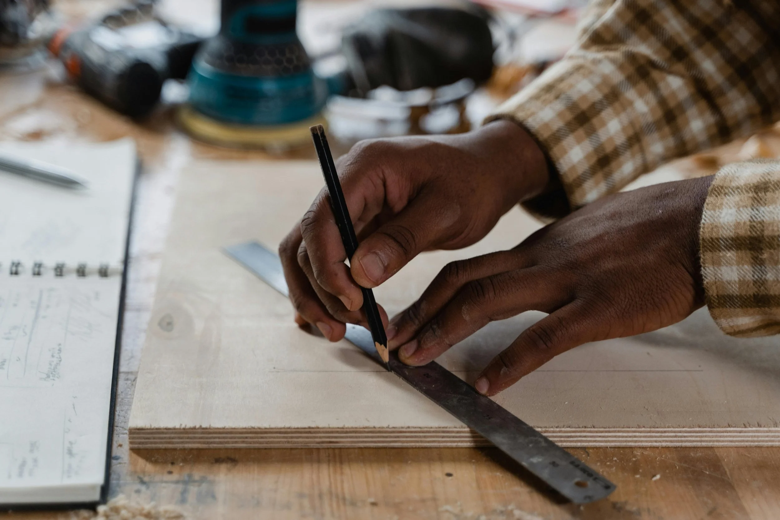 Hands measuring and marking wood on a workbench.
