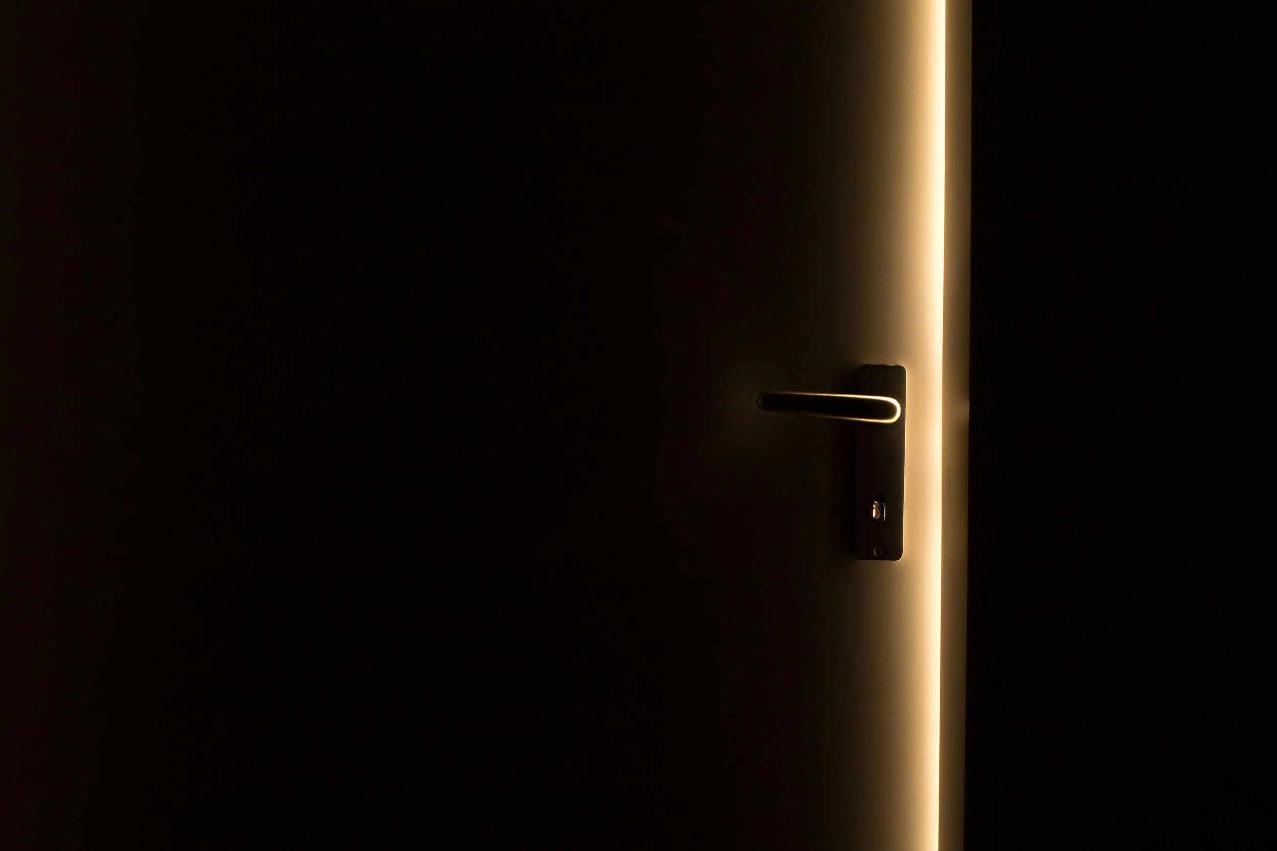 Door slightly open with warm light in a dark room.