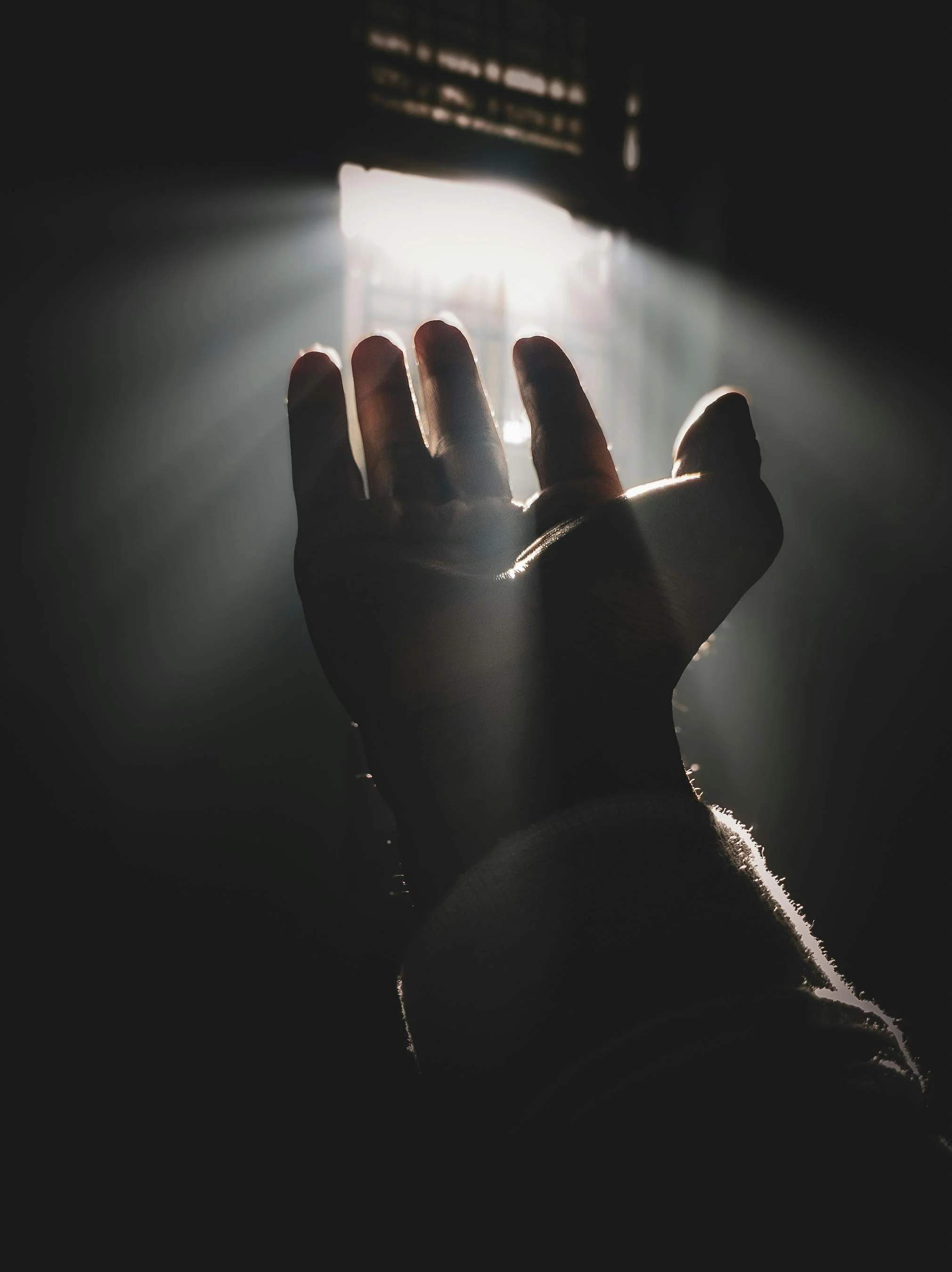 Outstretched hand reaching toward window light in a dark room.