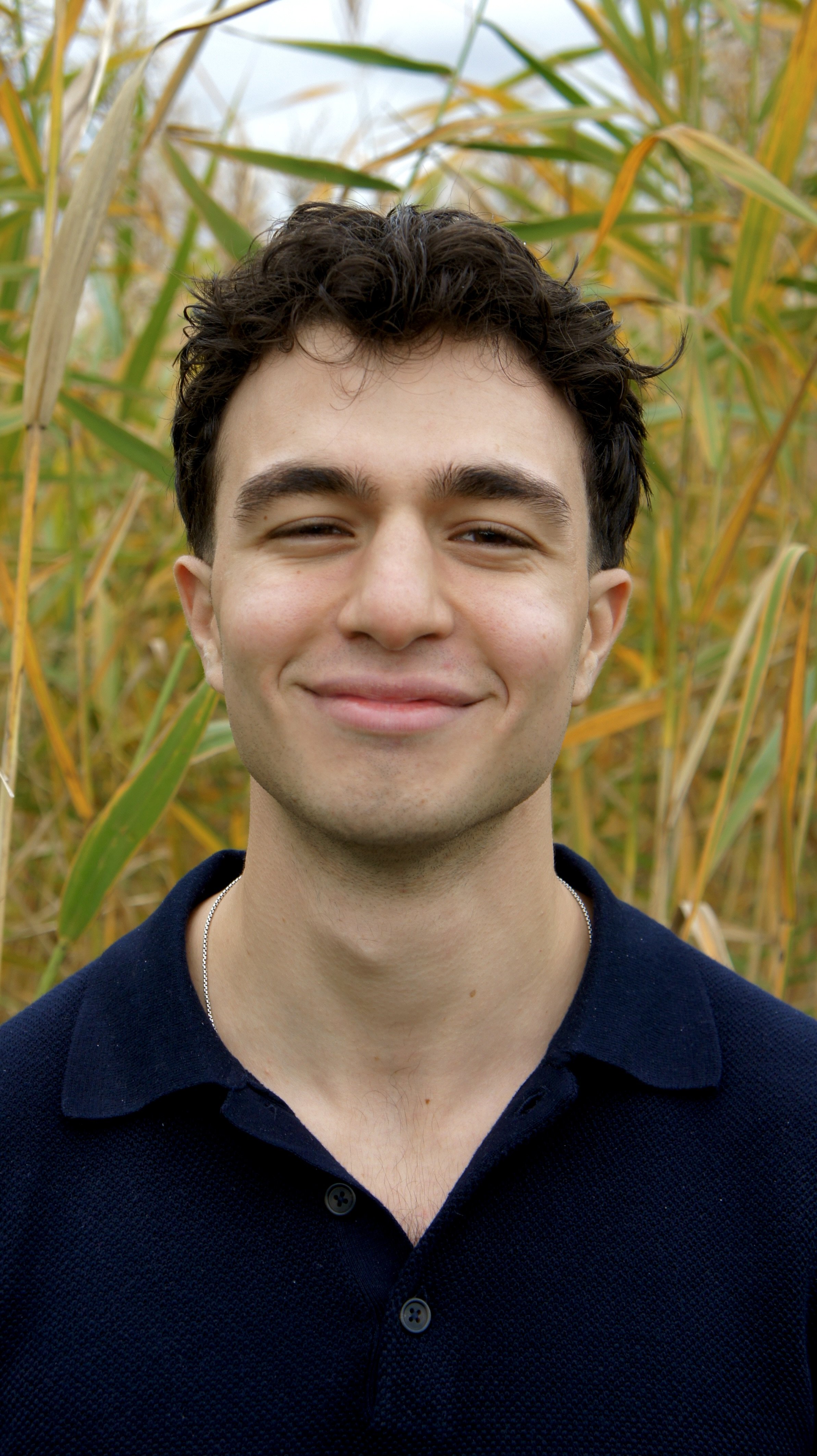 A young man smiling in a field of tall, yellowing grass or crops during the daytime.
