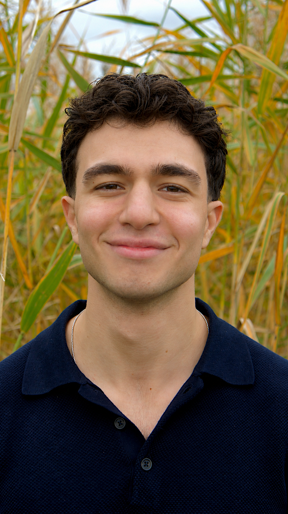A young man smiling in a field of tall, yellowing grass or crops during the daytime.