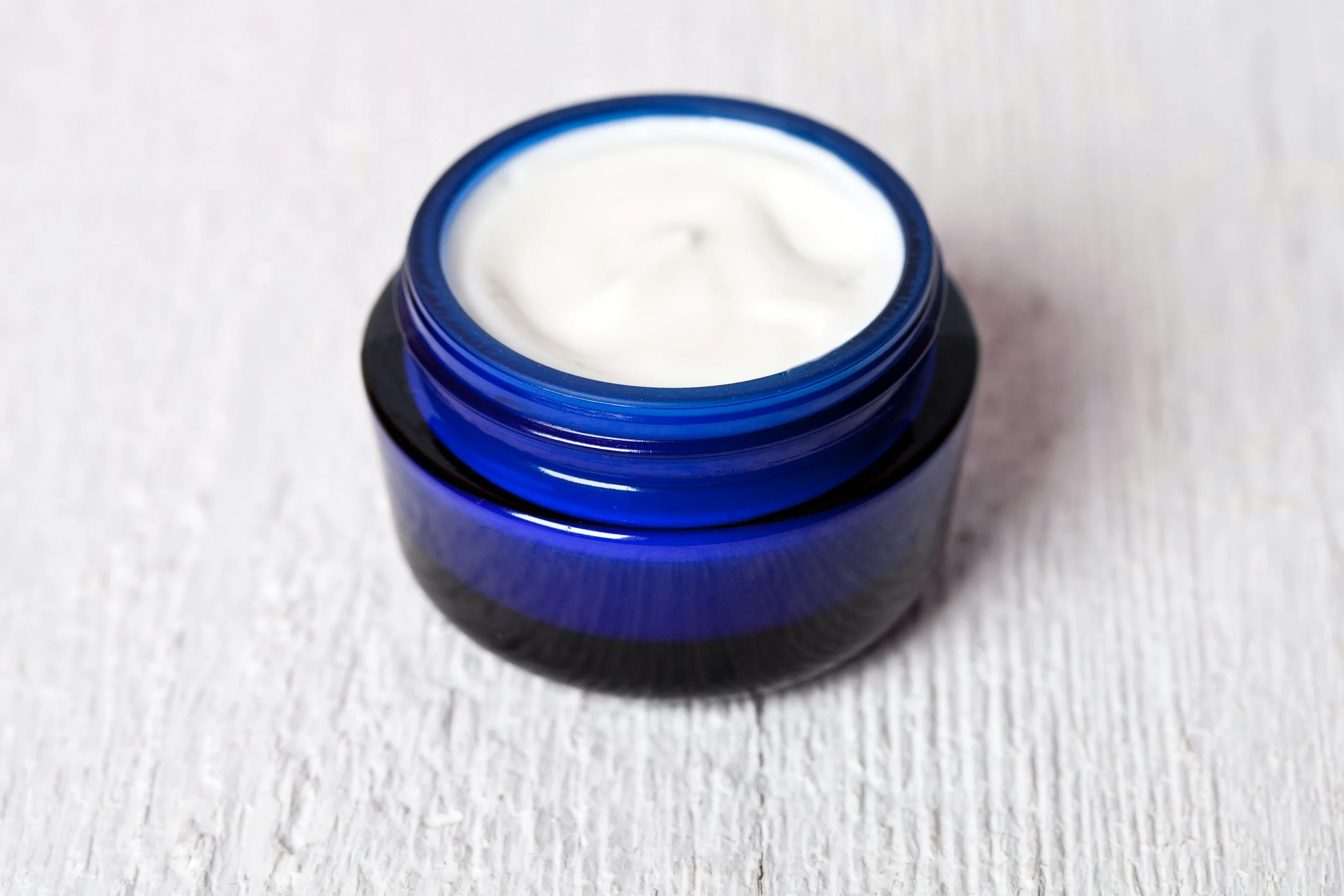Open blue jar of white cream on white surface.
