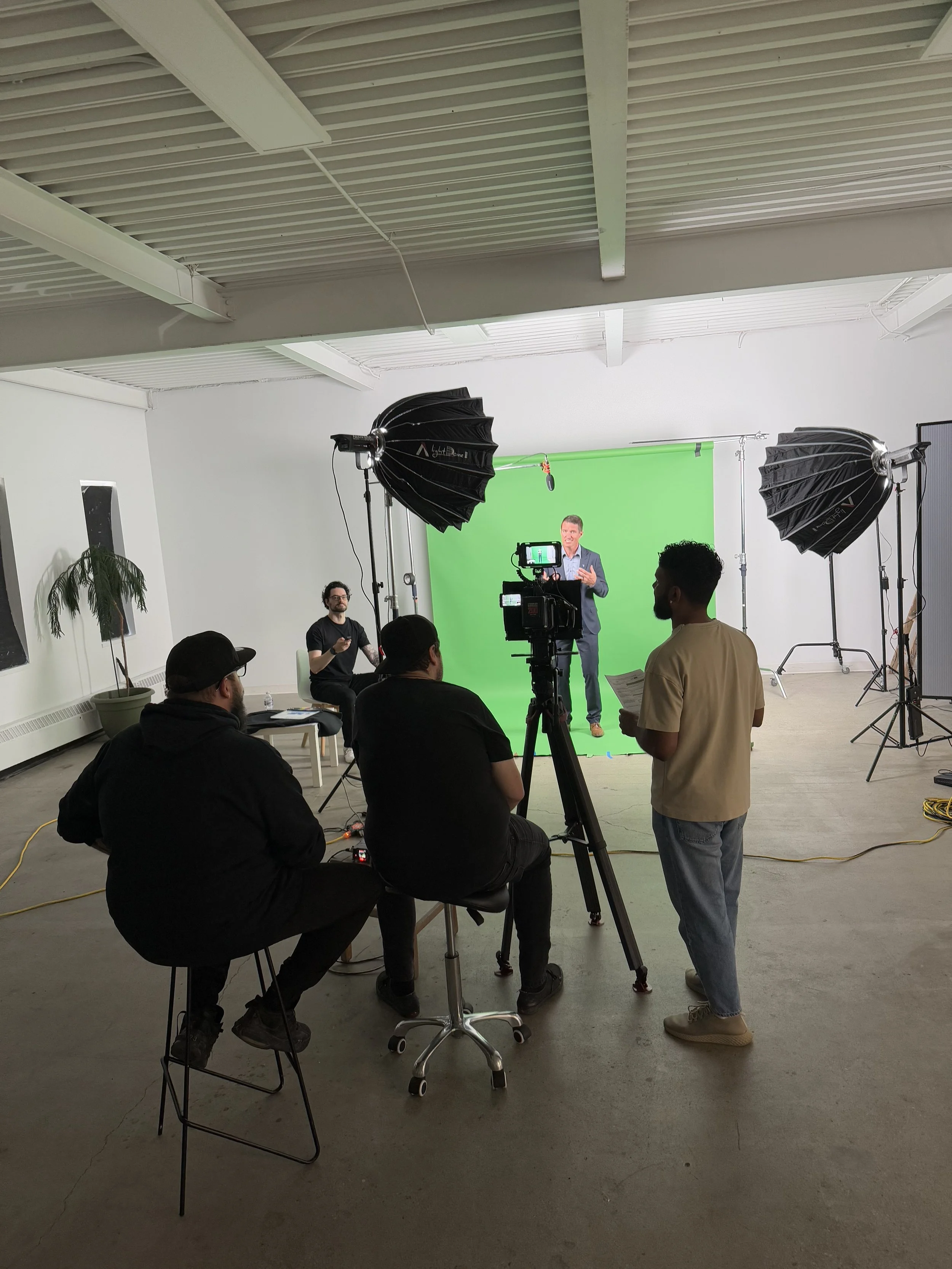 Group of people filming a man speaking in front of a green screen with professional studio lighting.