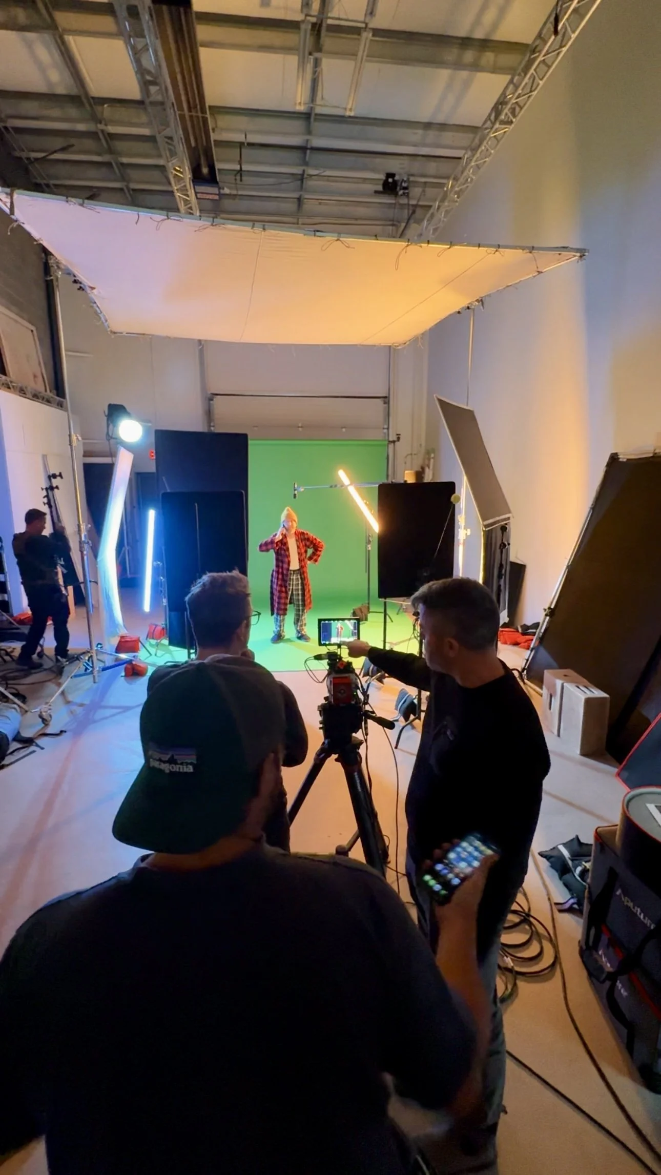Film crew filming a person in a colorful outfit against a green screen in a studio with equipment and monitors.