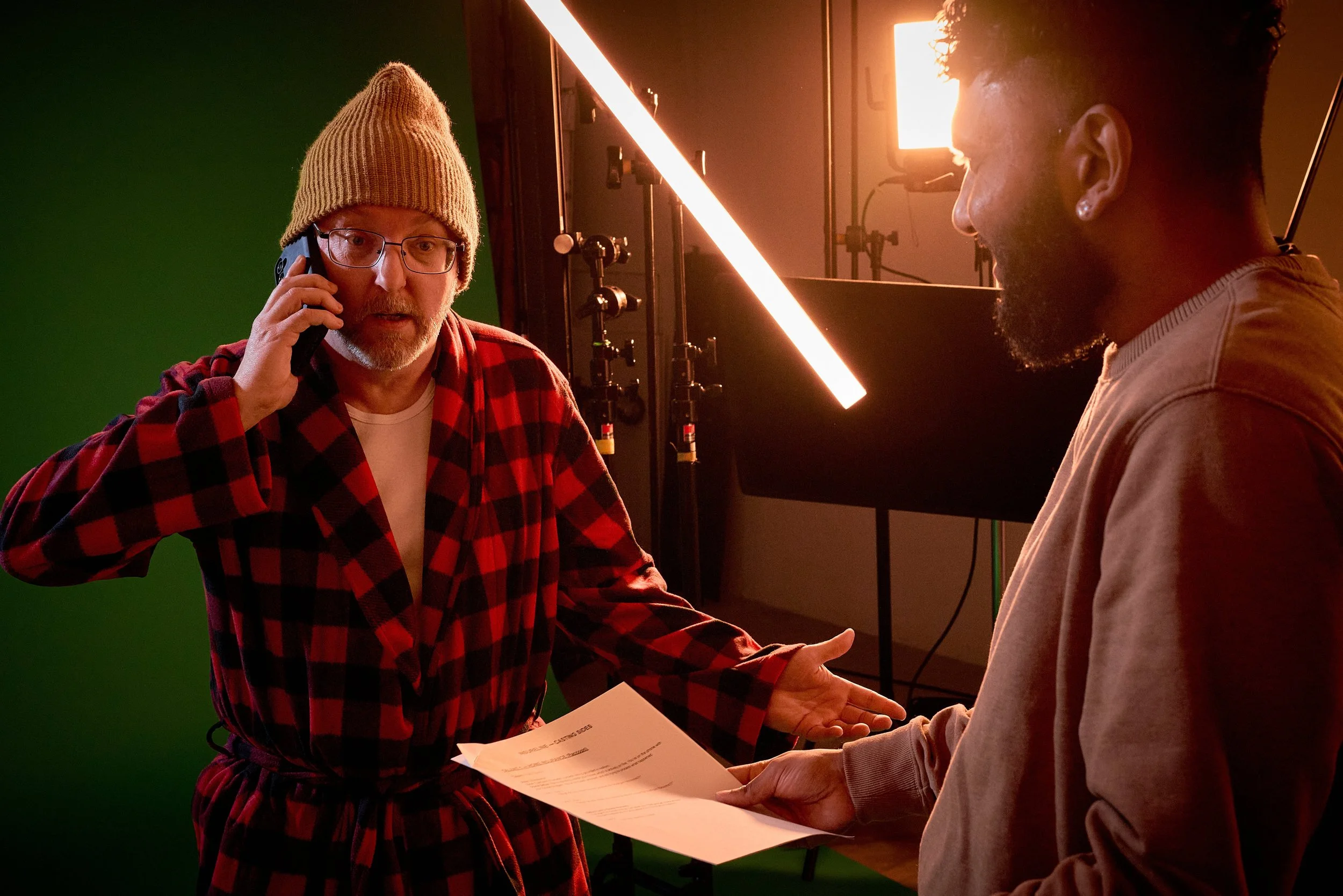 Two men exchanging documents and handshaking in a studio with green screen and professional lighting.