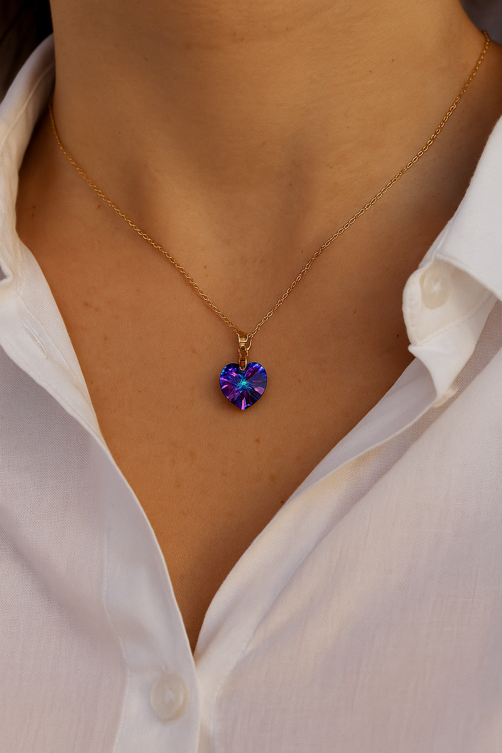 Close-up of a person wearing a gold chain necklace with a purple, heart-shaped pendant, partially visible white button-up shirt.