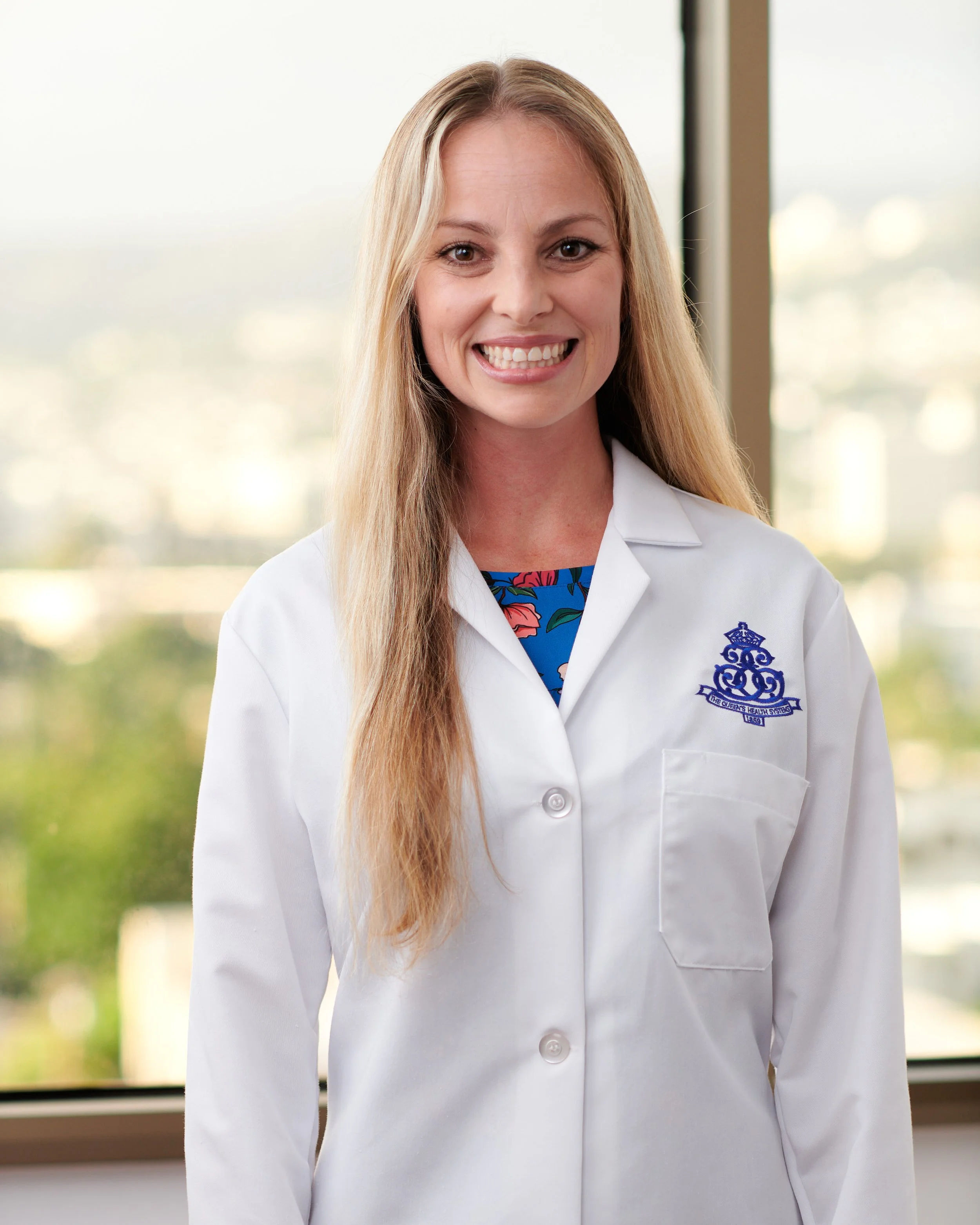 A smiling woman in a white lab coat standing in front of a window.