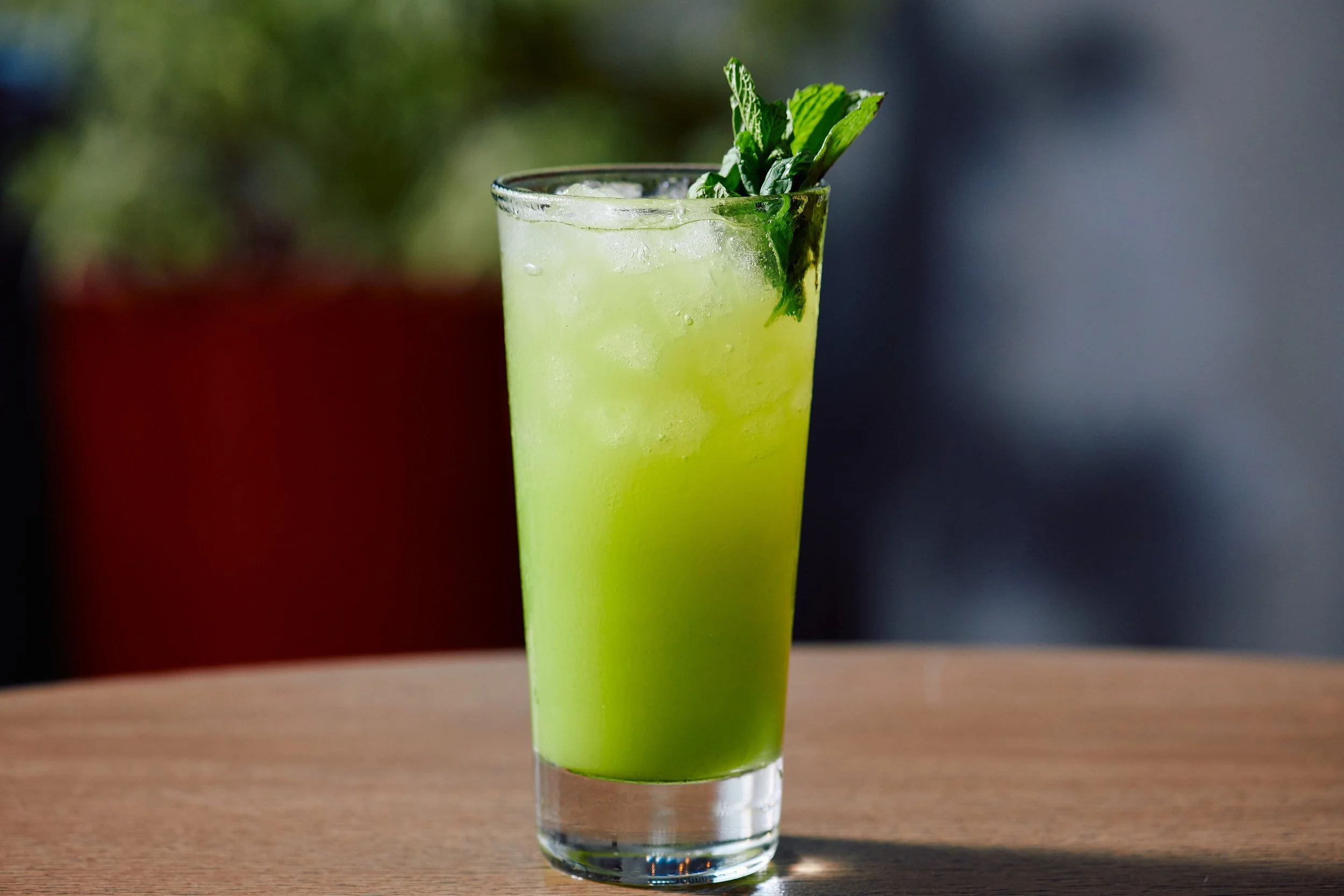 A tall glass of green beverage with ice, garnished with fresh mint leaves and a lime wedge, on a wooden table.
