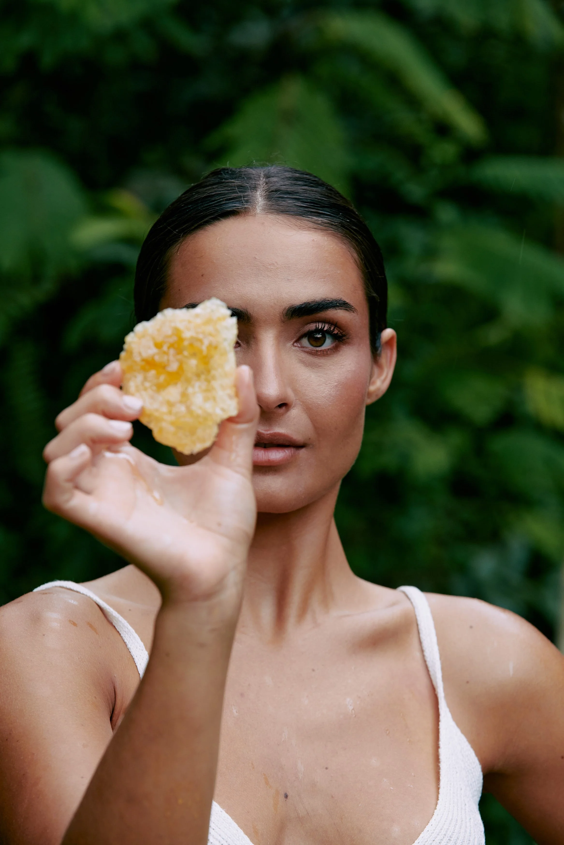 Woman with wet hair holding a piece of bread in front of her face, with a jungle background.