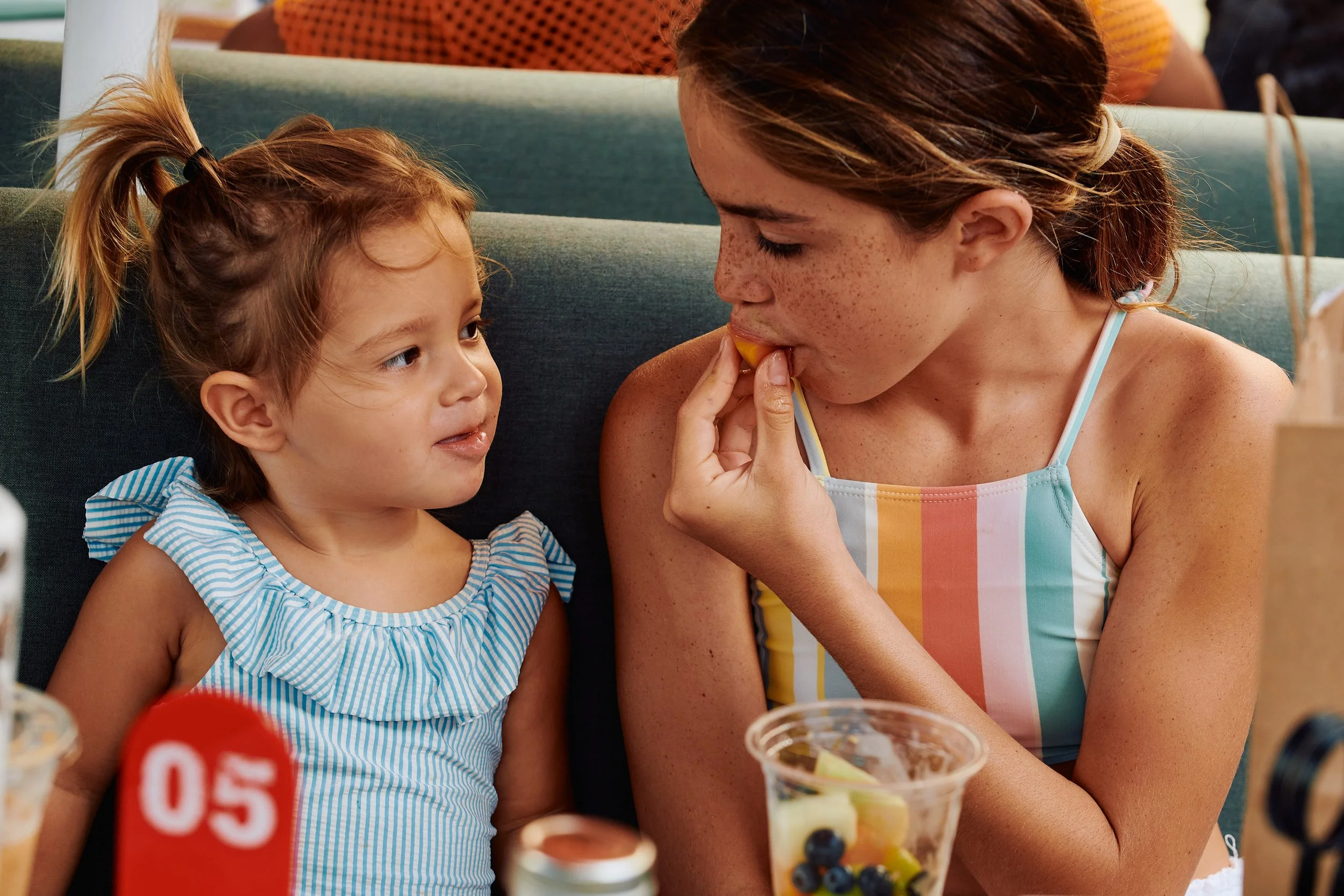 A woman and a young girl sharing a lemon slice at a restaurant table with desserts and drinks.