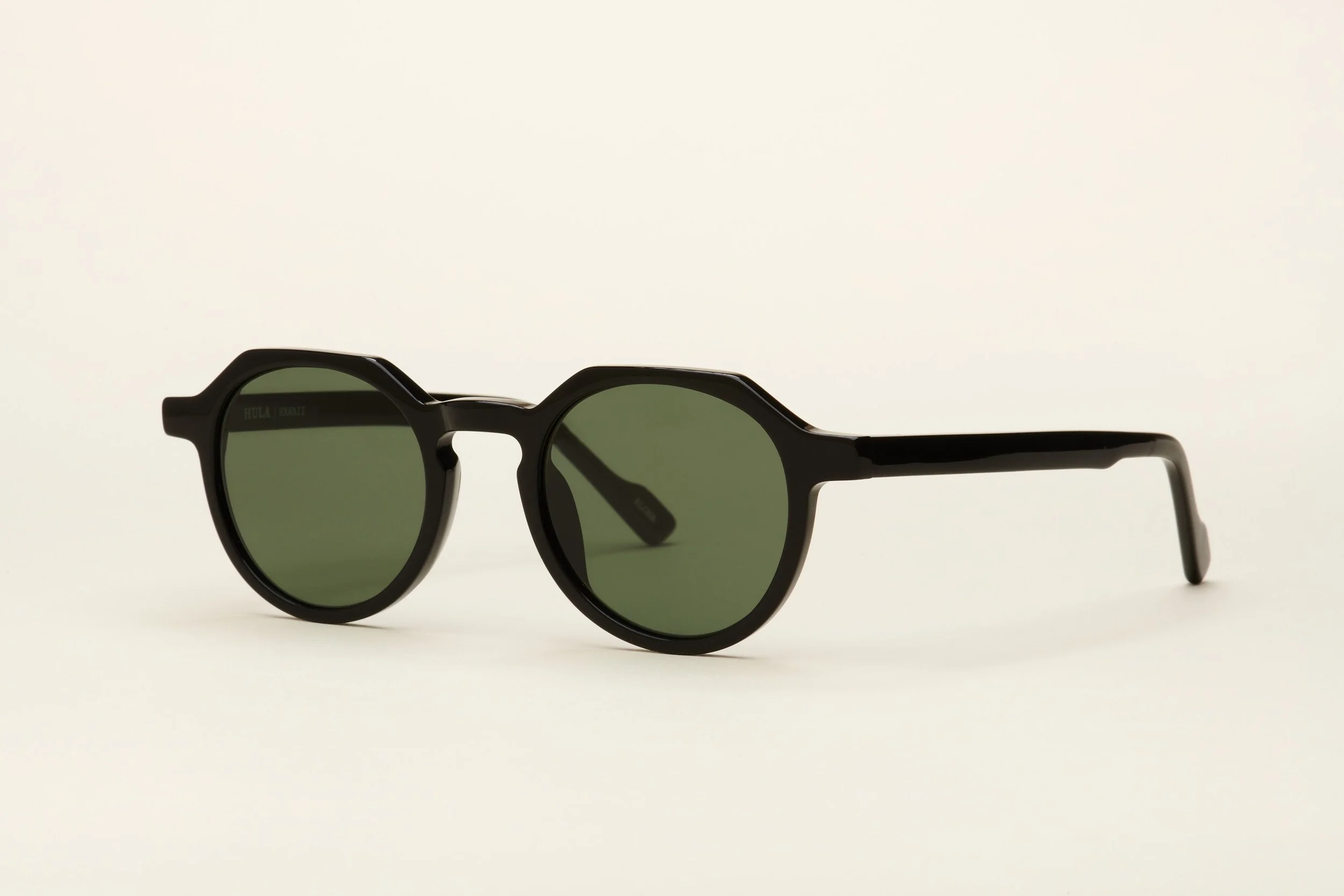 Black round sunglasses with dark green lenses on a plain light background.