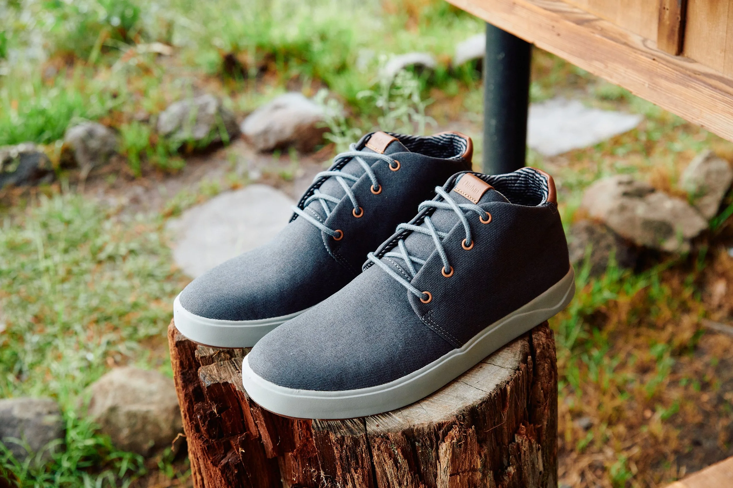 A pair of gray and black casual sneakers with white soles resting on a tree stump outdoors.