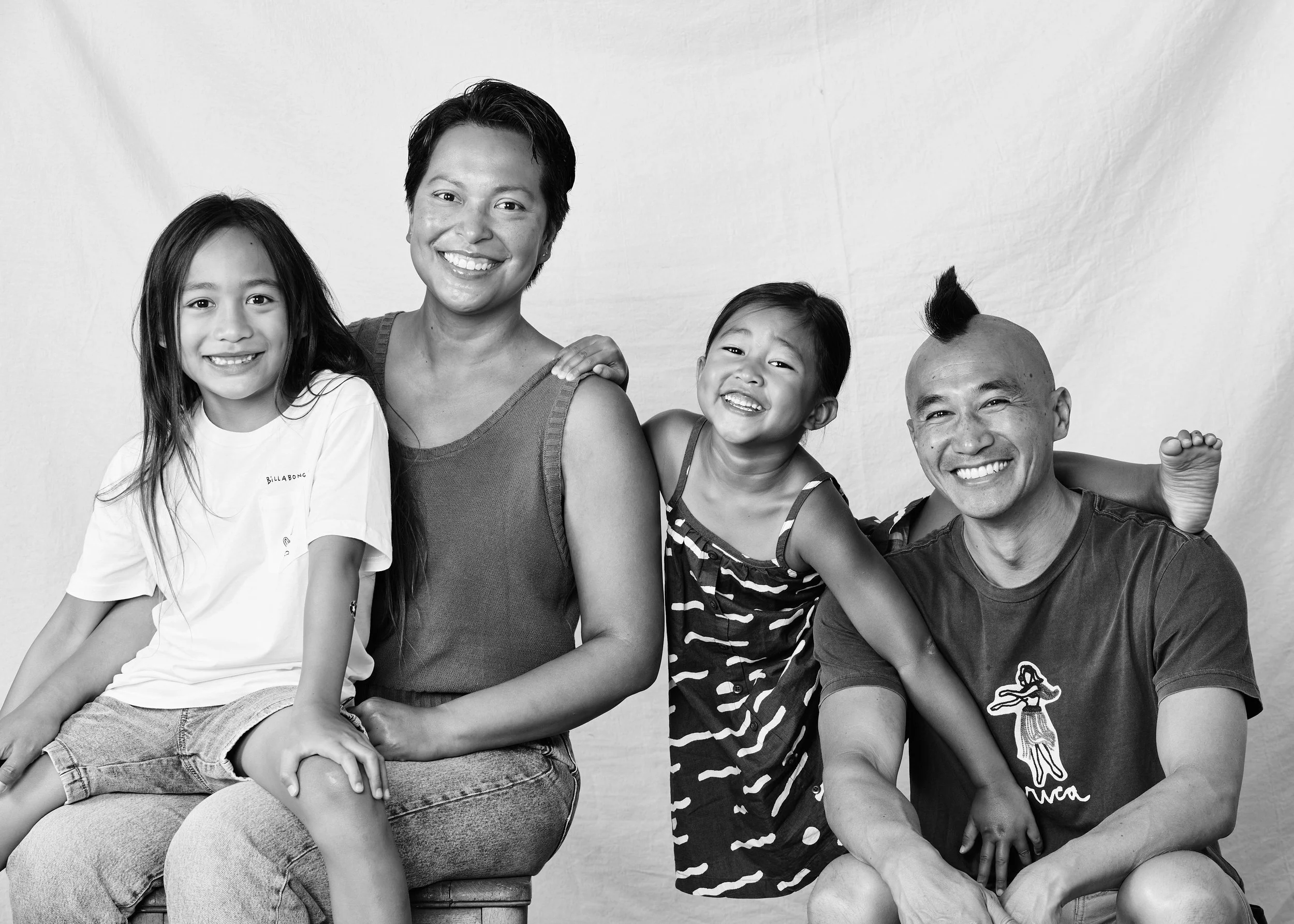 Black and white photo of a diverse family of four smiling together, sitting against a plain backdrop.