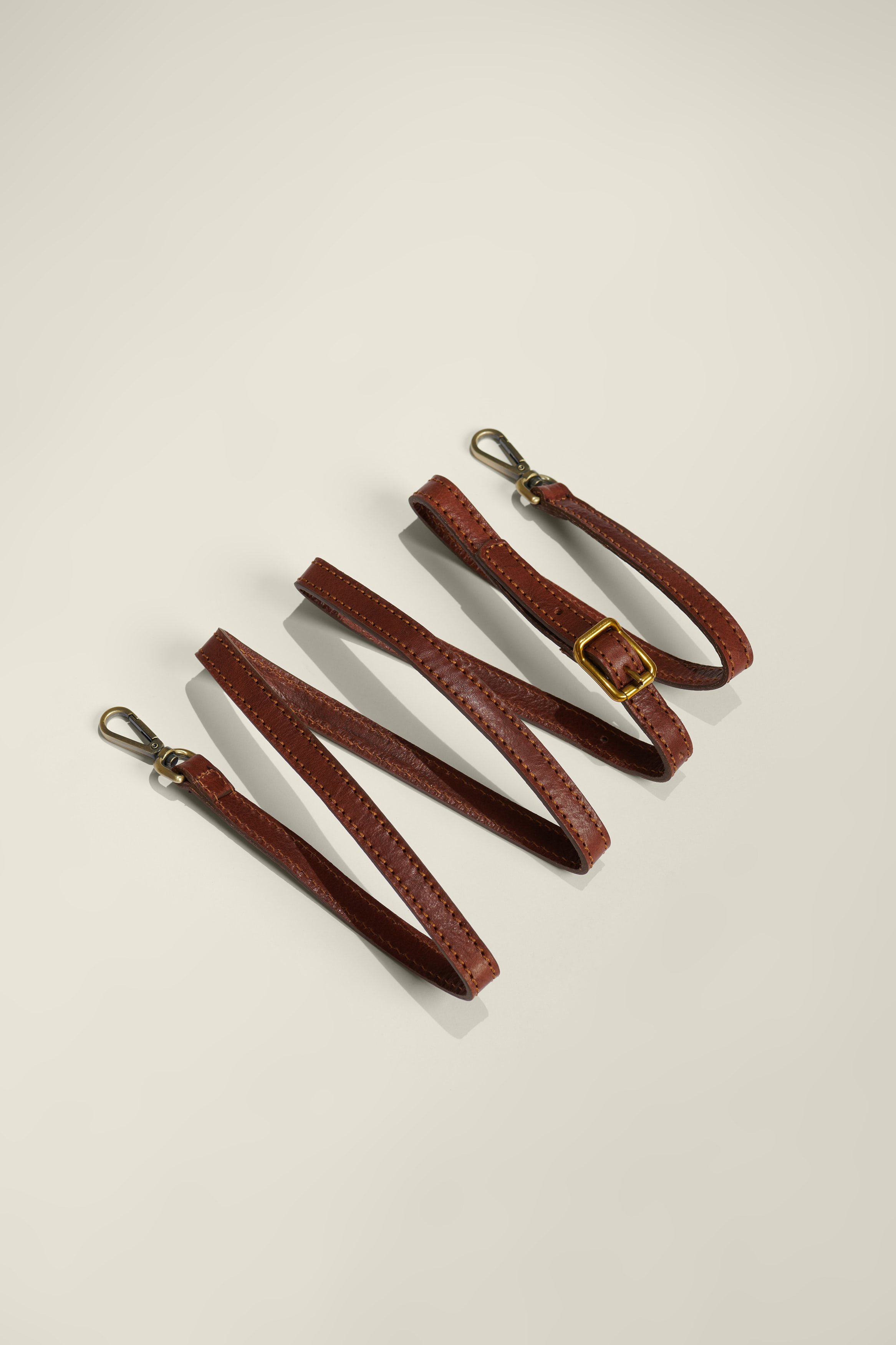 Three brown leather dog collars with metal clasps lying on a white surface.