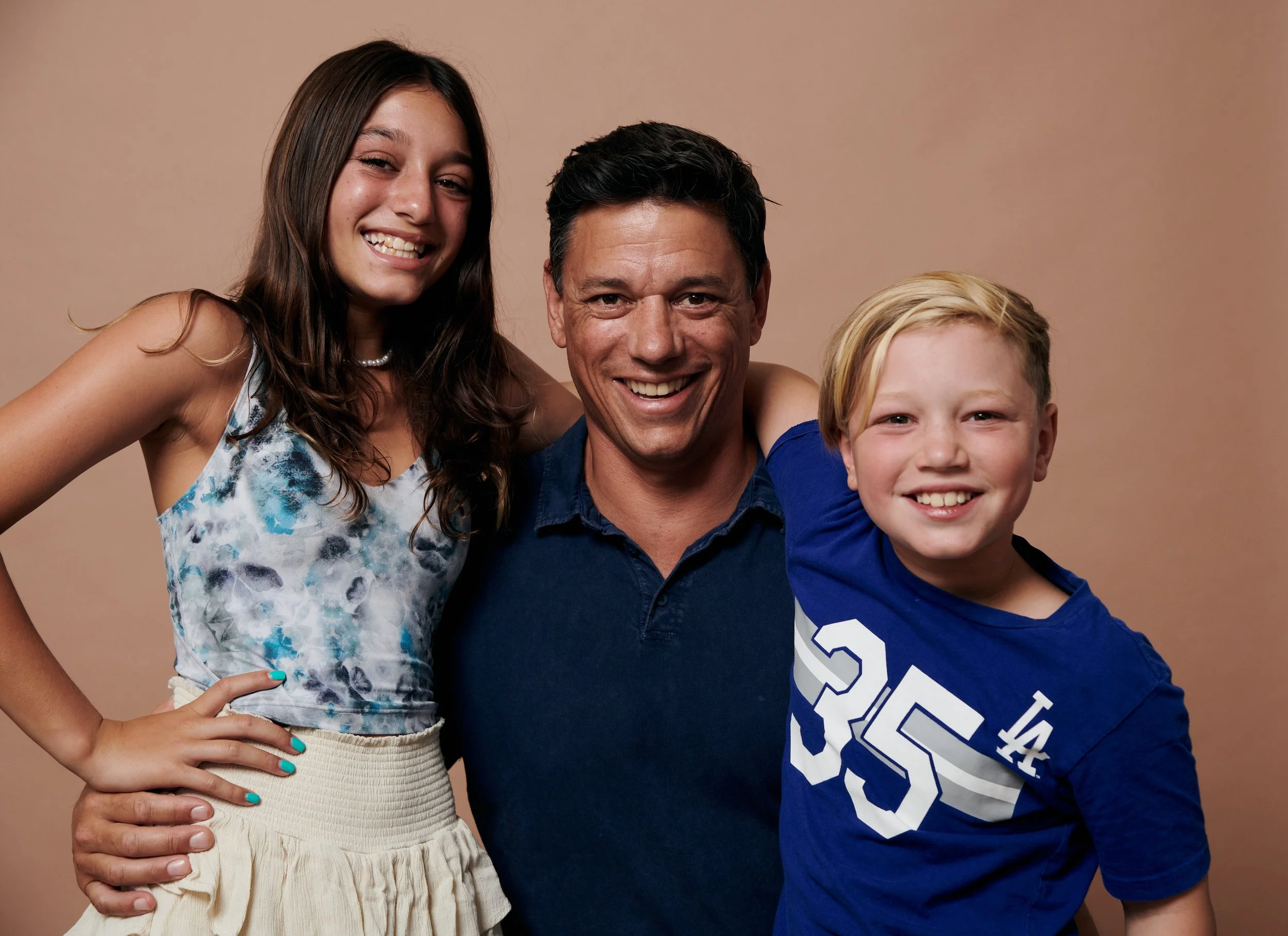 A smiling woman, man, and young boy posing together with a beige background.